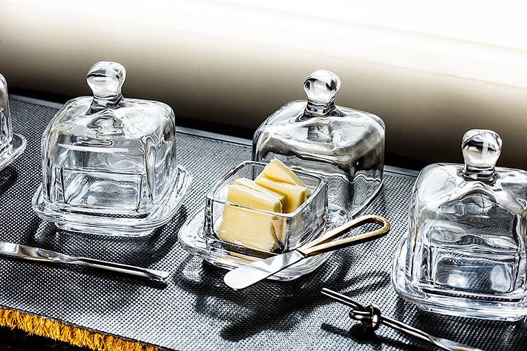 Clear glass butter dishes with lids on a metallic surface