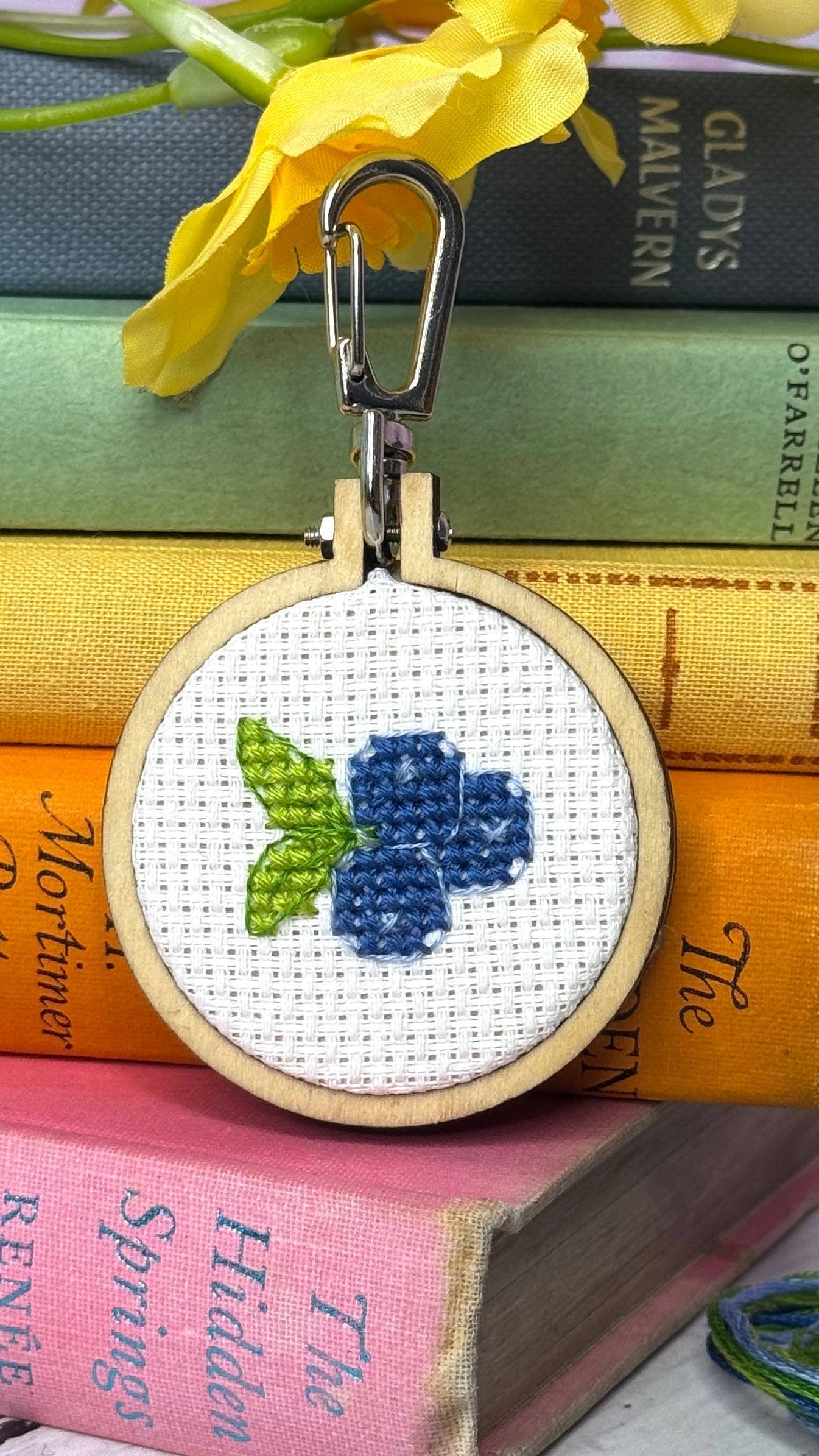 Cross-stitched keychain with blueberries on a stack of books