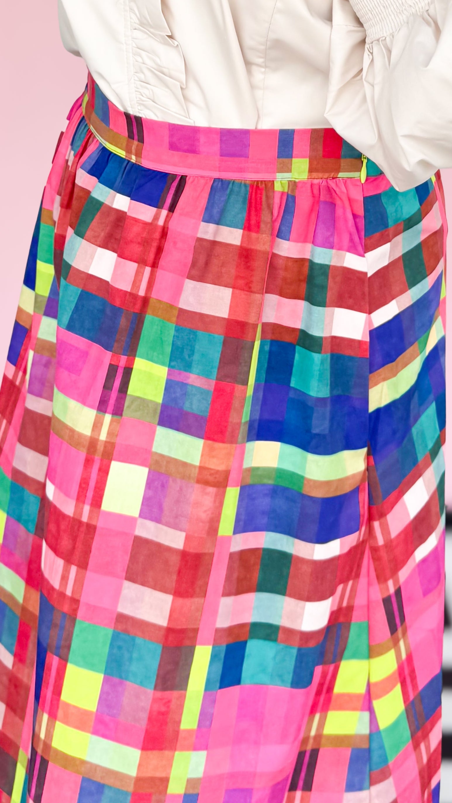 Person wearing a white blouse and colorful plaid skirt against a pink background