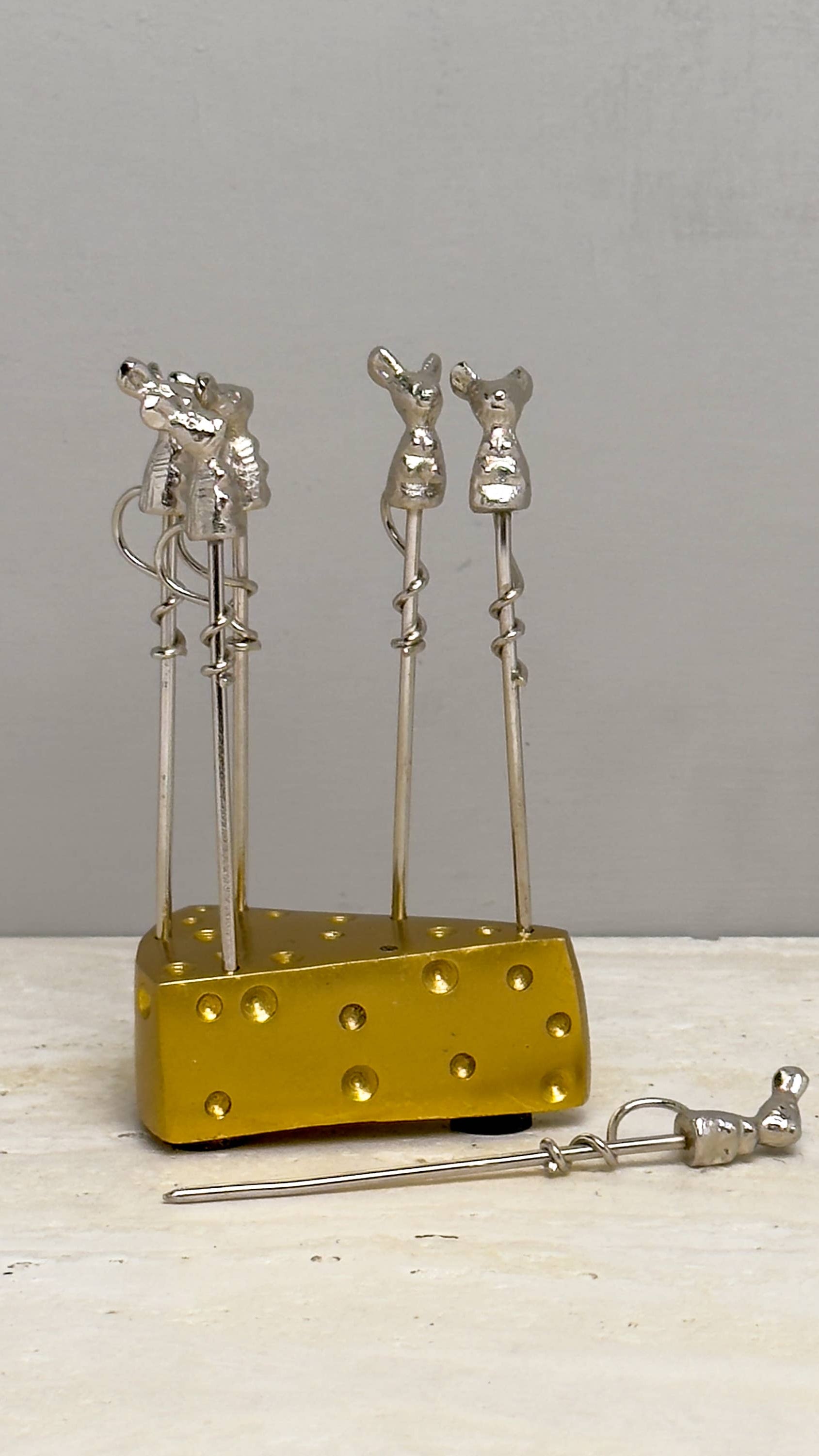 Metal skewer holder with three skewers on a wooden surface and gray background
