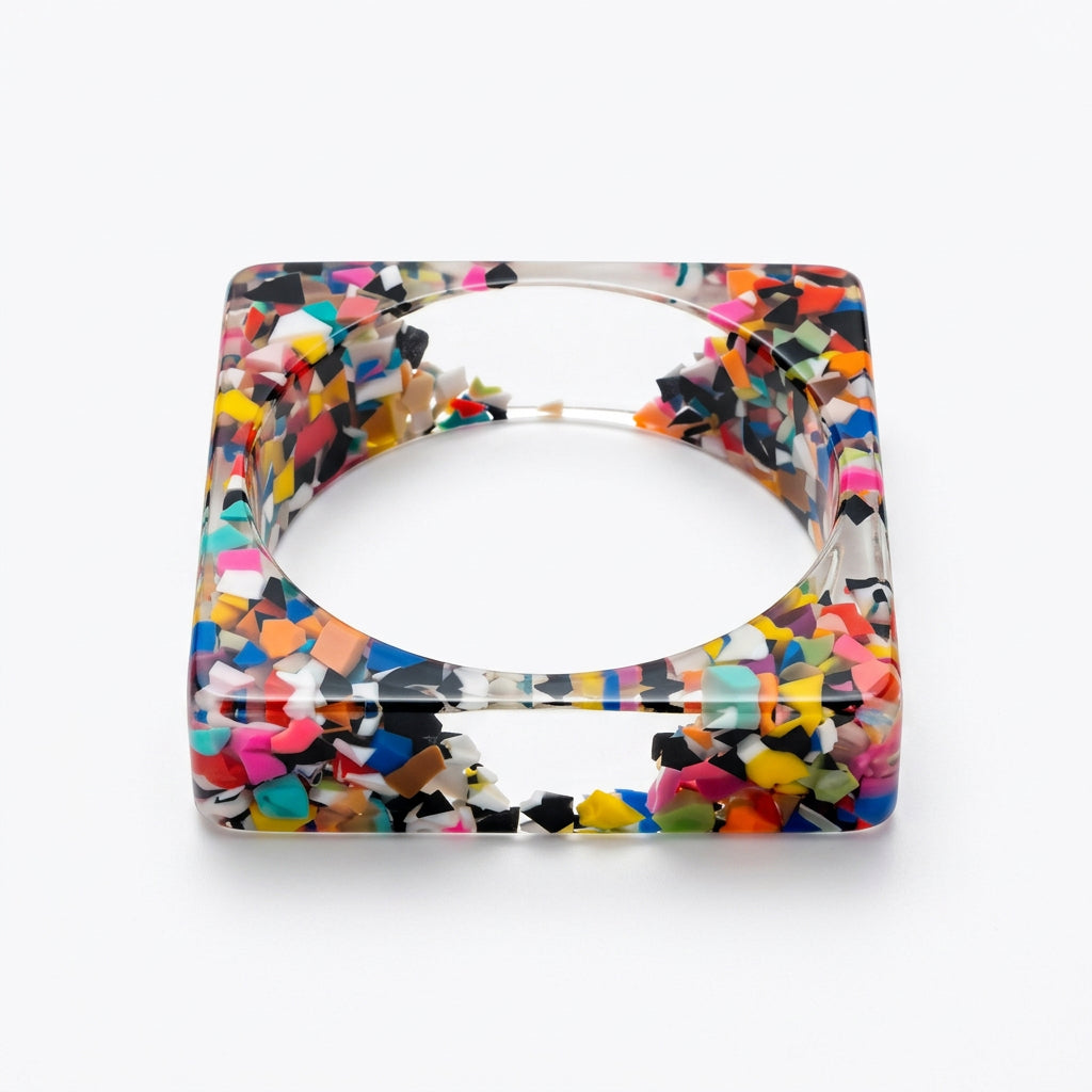 Square clear resin bangle bracelet filled with multicolor confetti pieces in pink, yellow, blue, teal and black, angled view.