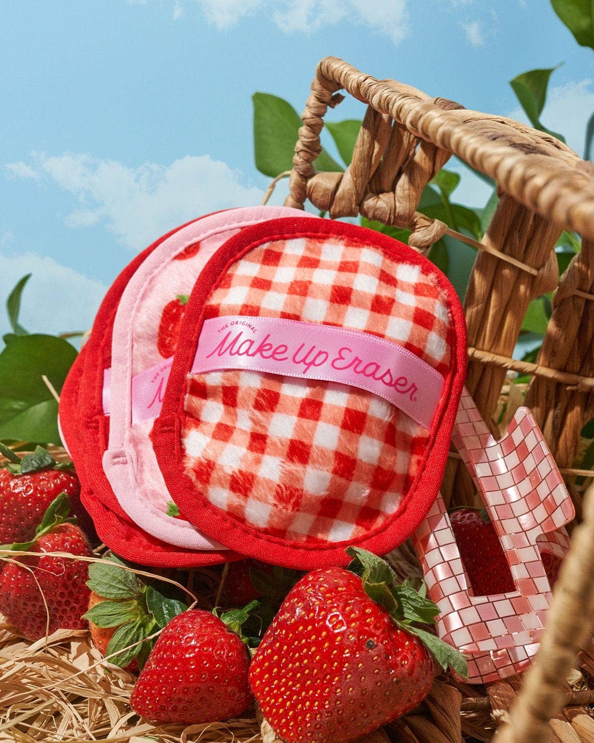 Makeup eraser with red and white checkered design and pink band in a basket with strawberries