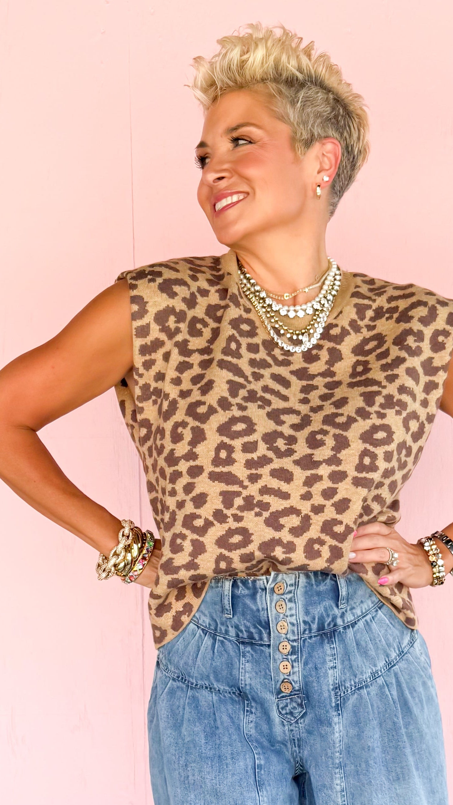 Person wearing a leopard print top and blue jeans against a pink wall with a geometric floor.