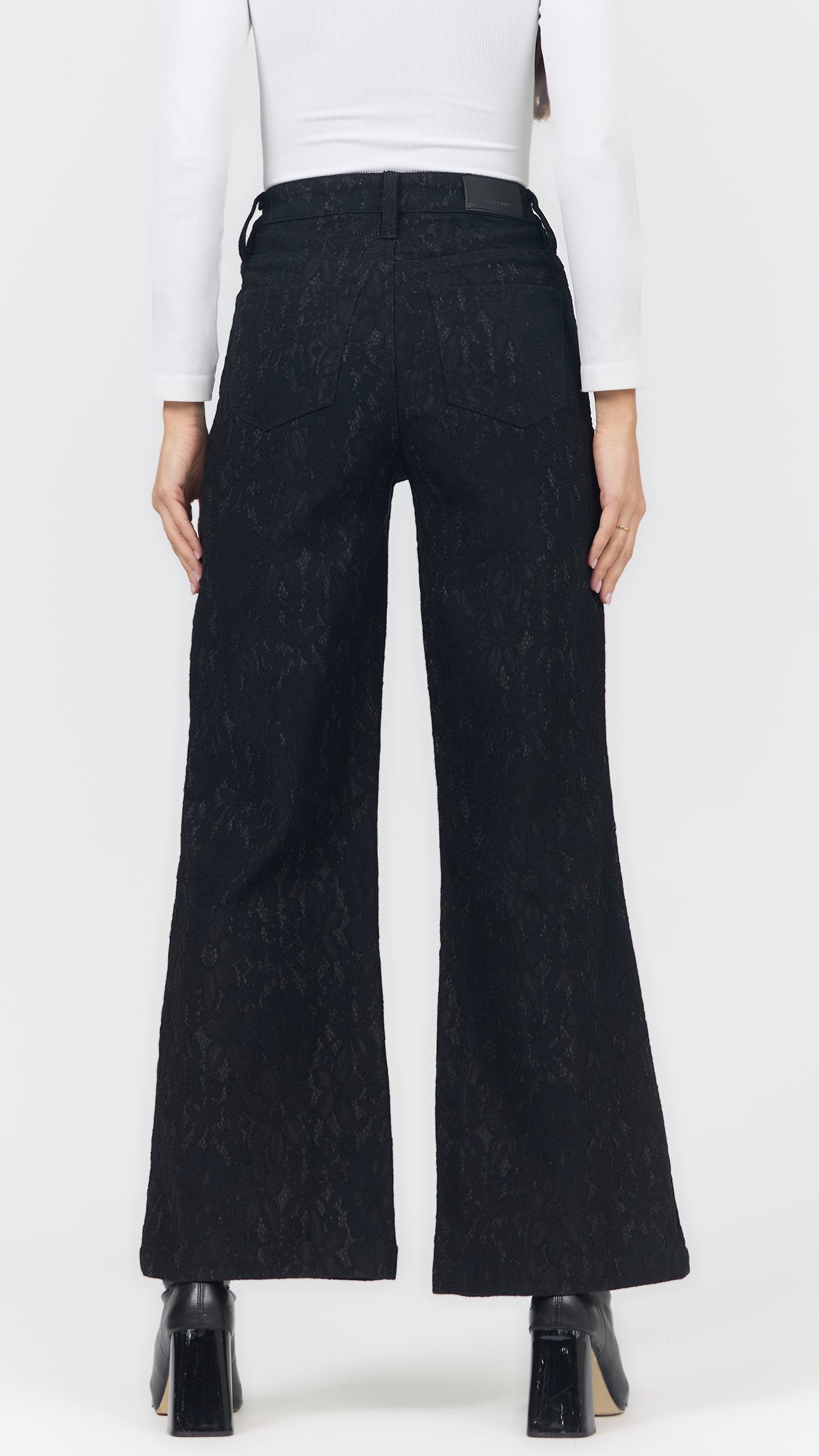 Back view of black lace wide leg pants showing the back pockets, leather waistband patch, and black ankle boots
