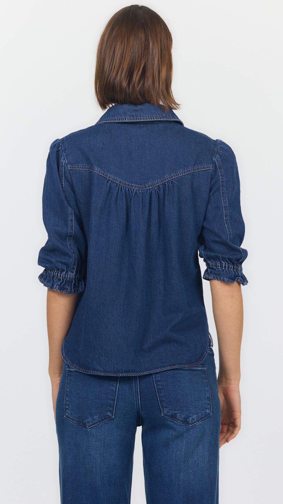 Back view of dark cobalt denim blouse showing the gathered back yoke and ruffled elbow cuffs