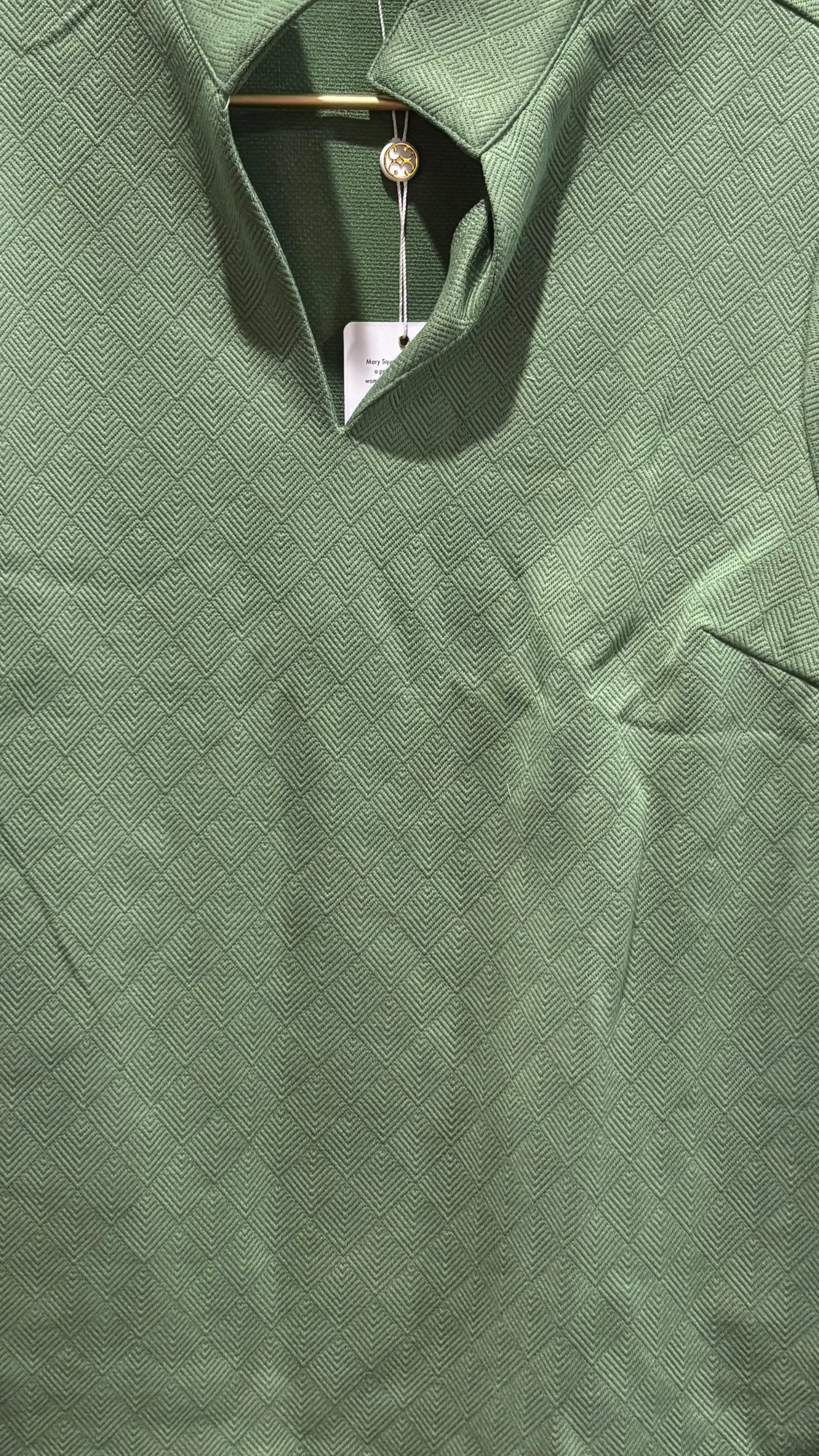 Green fleece pullover on a hanger with a cluttered background