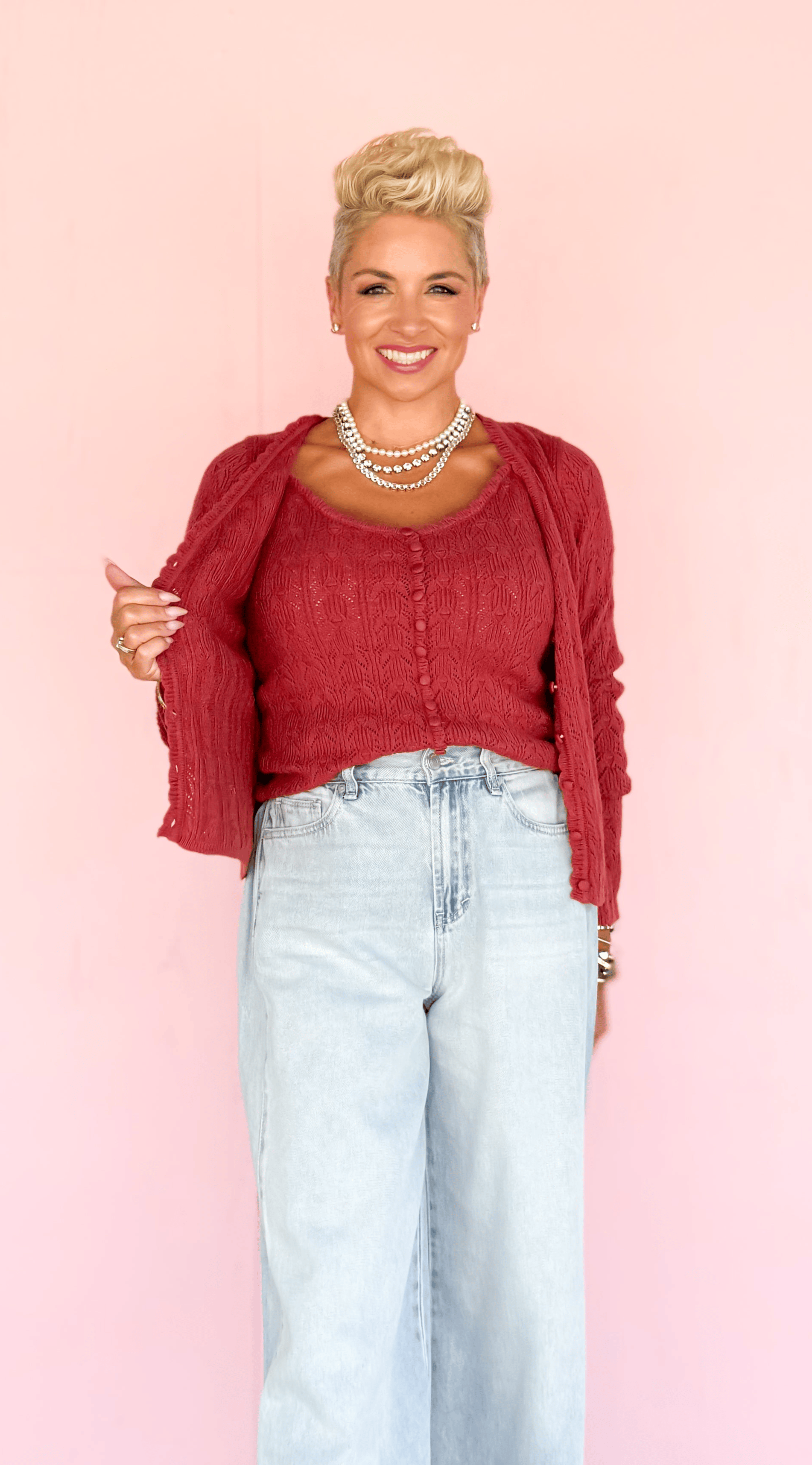 Person wearing a red cardigan and light blue jeans against a pink background