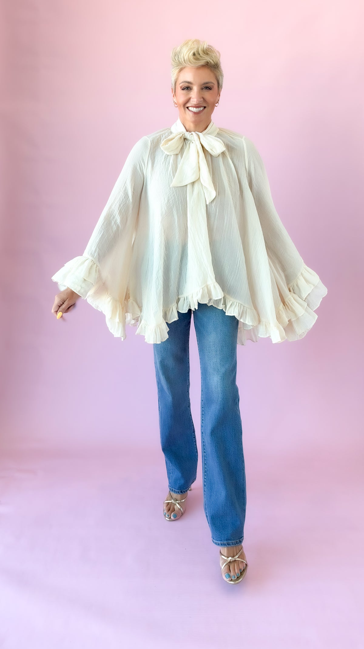 Cream oversized bow blouse shown with arms extended to display the flowing silhouette