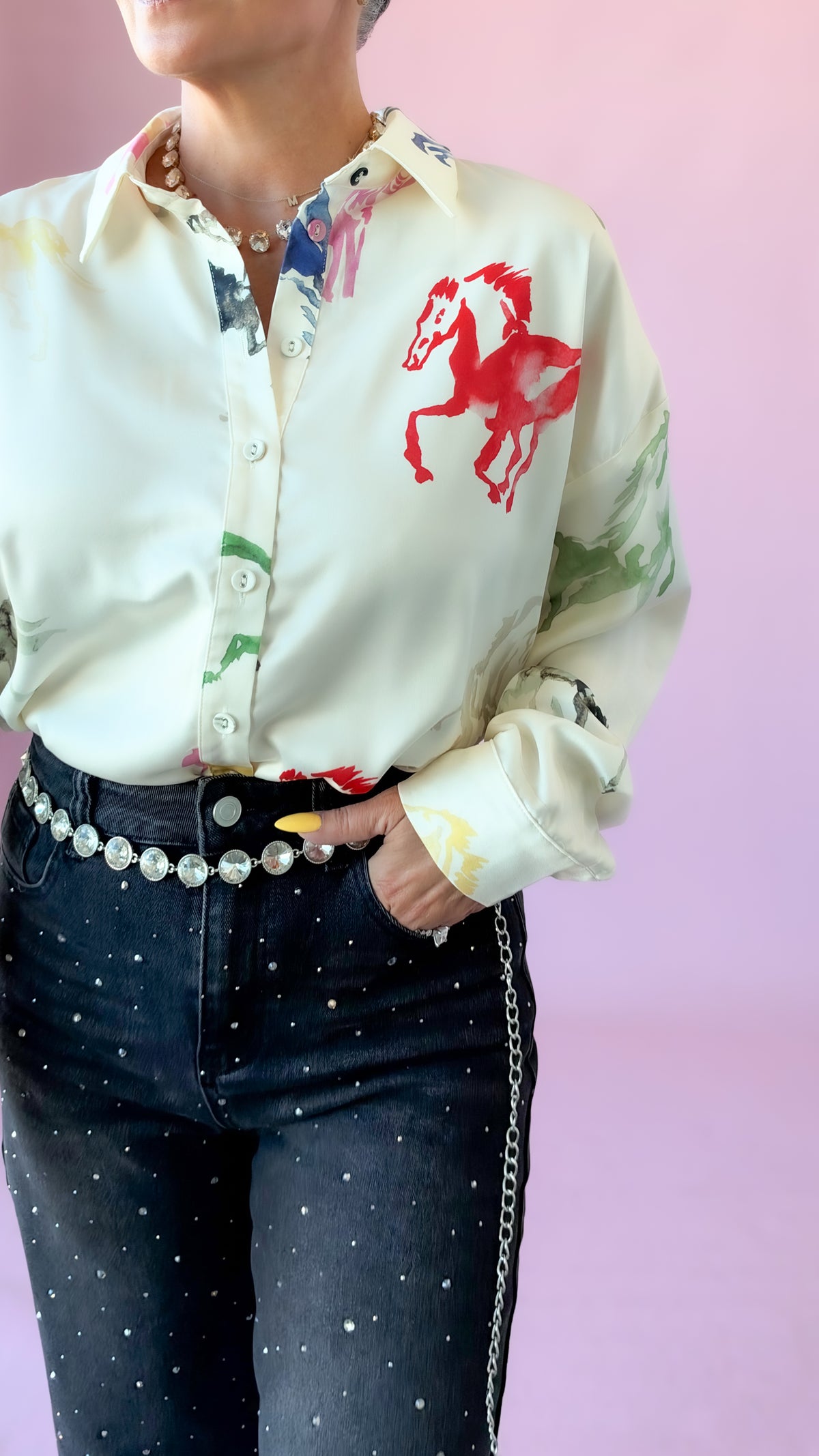 Close-up of cream satin blouse with red watercolor horse print, worn with studded jeans