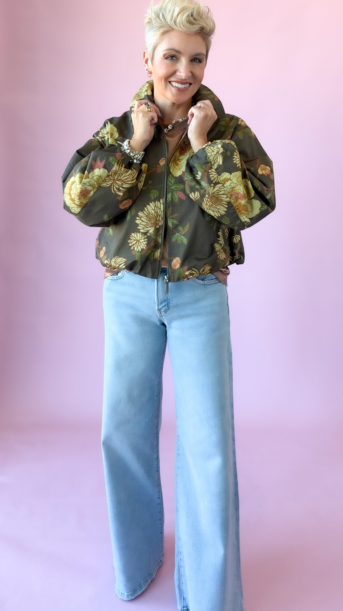 Model holding the collar of an olive floral cropped jacket worn with wide-leg jeans