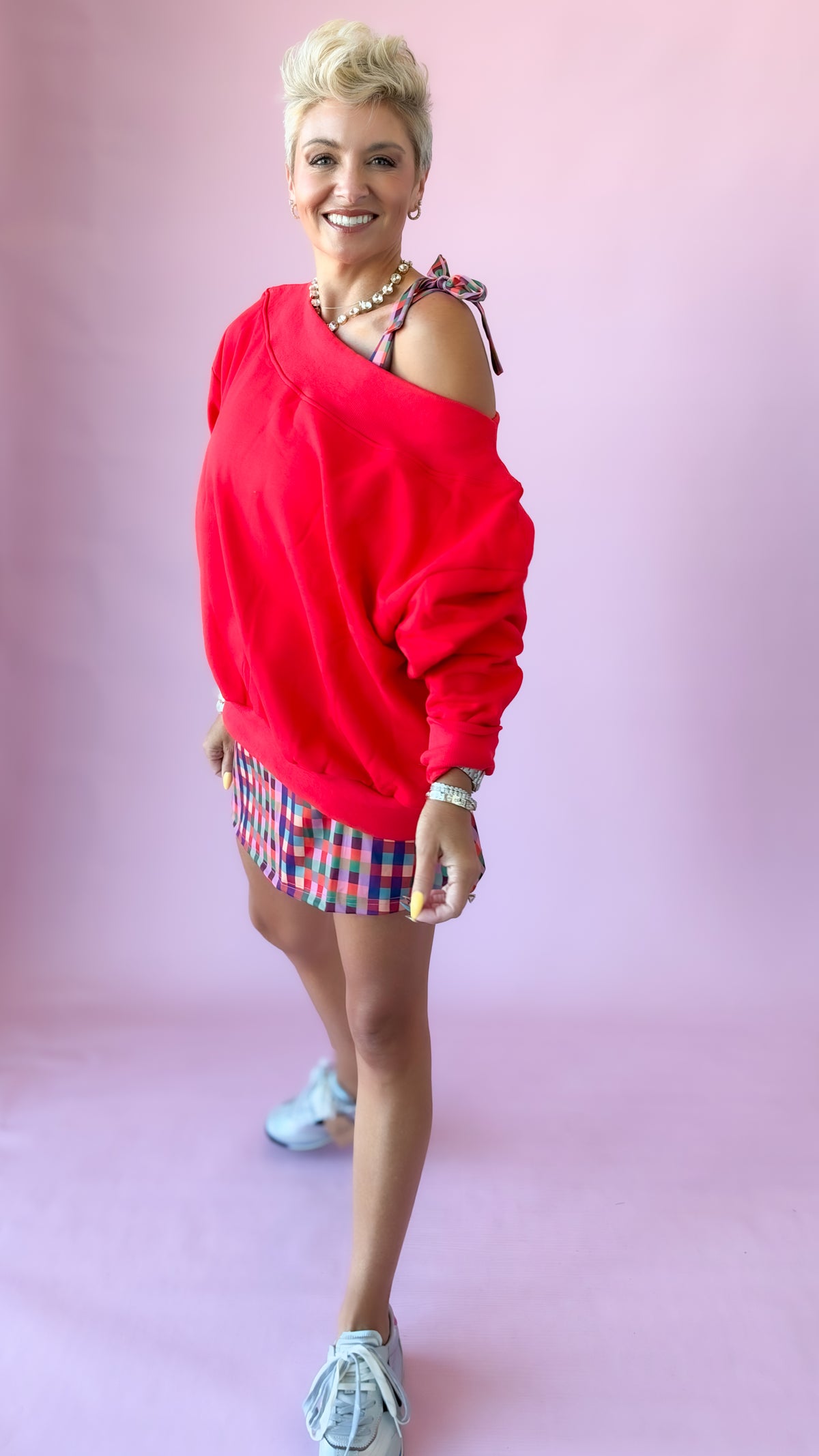 Red Harlow off-shoulder sweatshirt with plaid shorts and sneakers, mid-stride