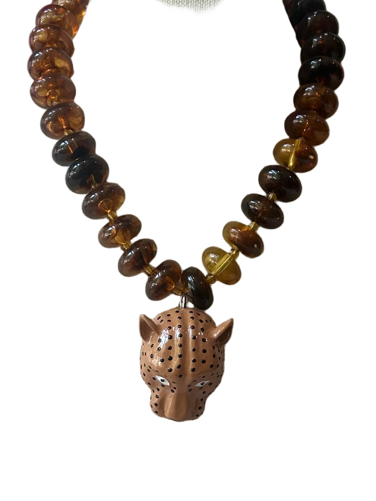 A beaded necklace with brown and black round beads and a carved brown animal head pendant, displayed on a white necklace stand against a white background.