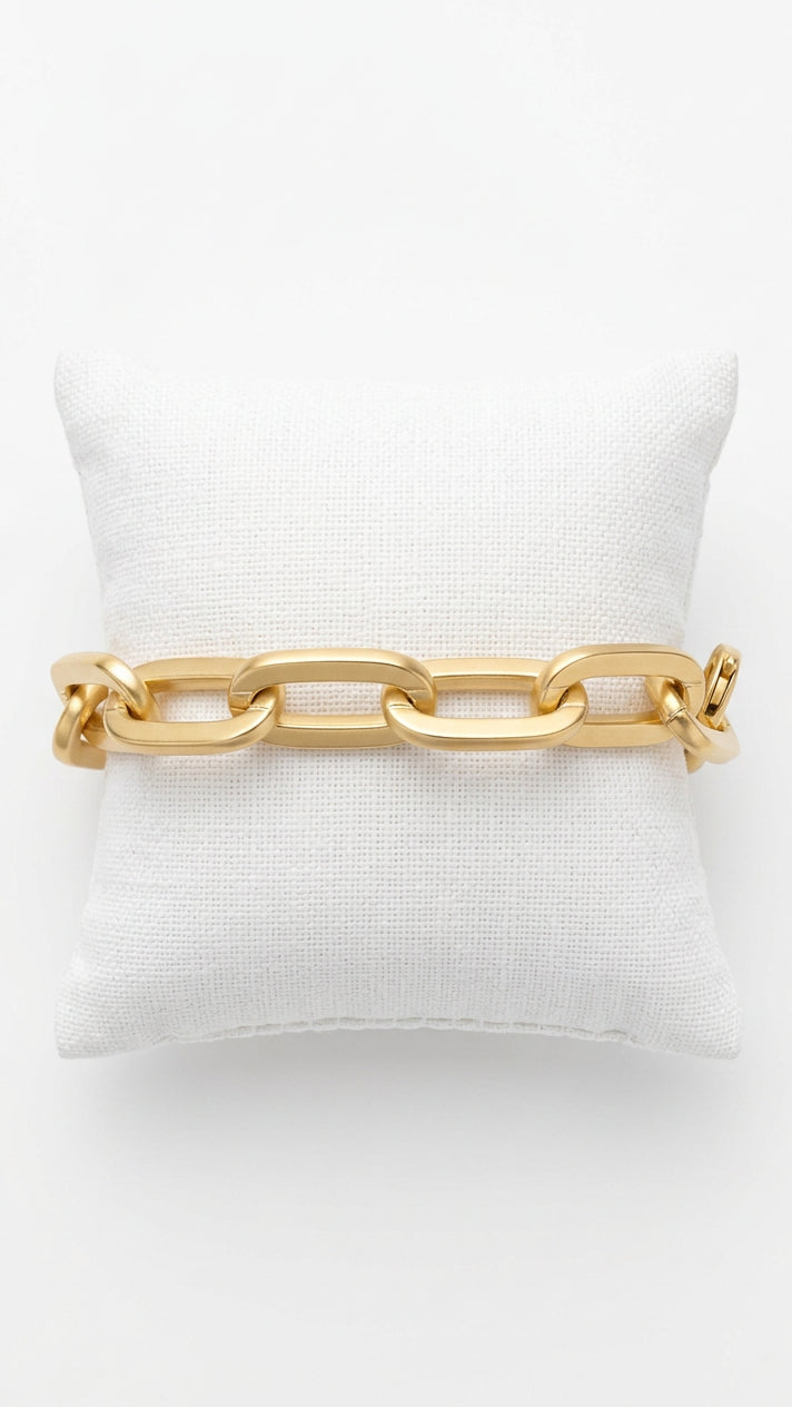 A chunky gold chain link bracelet displayed on a textured beige fabric.