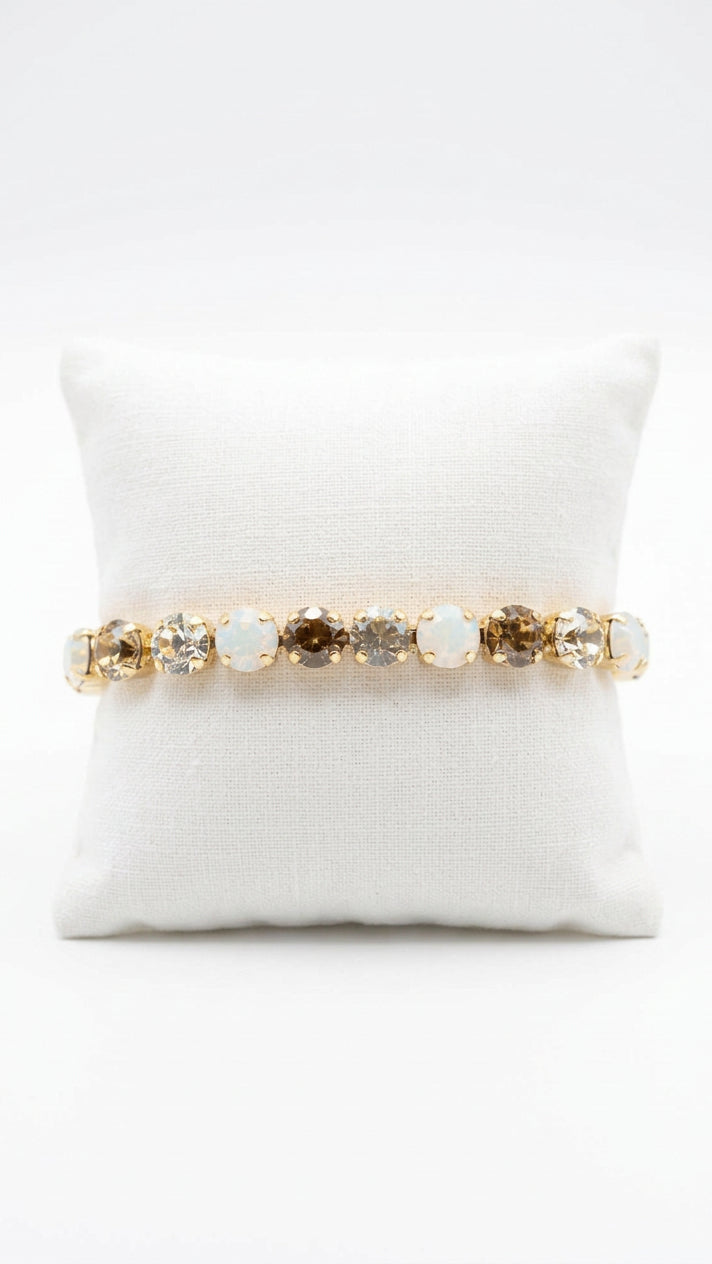 Stretch bracelet with round champagne-colored faceted stones and milky white stones in gold-tone settings, displayed around a white jewelry cushion.