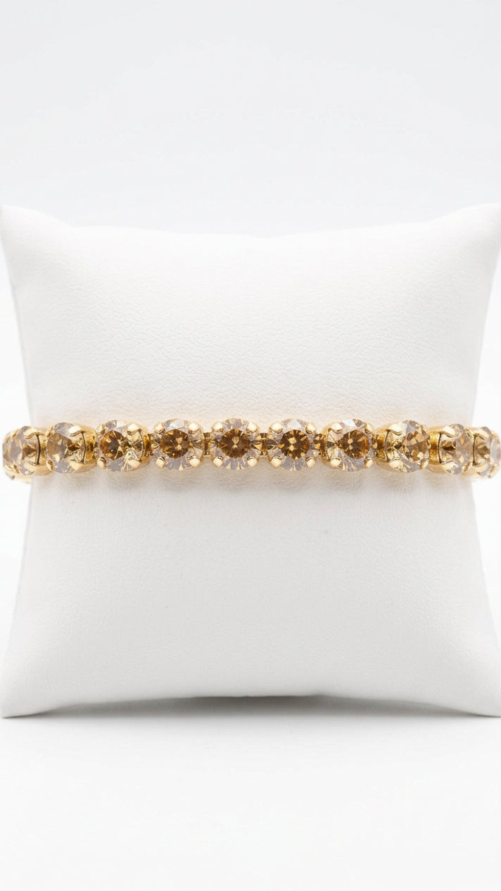 Champagne rhinestone stretch bracelet with a single row of round, faceted stones in gold-tone settings, displayed around a white jewelry cushion.