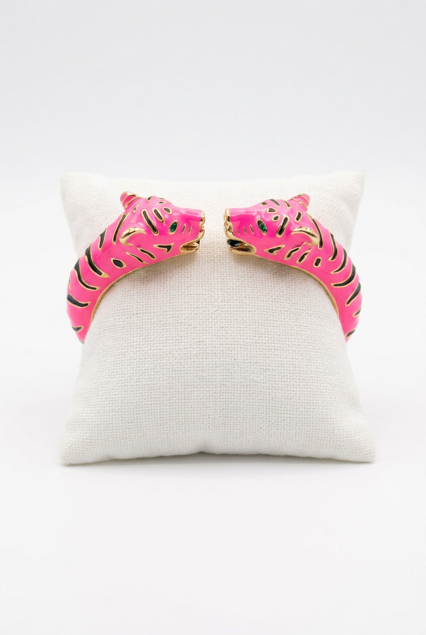 Hot Pink: Hot pink enamel cuff with two facing leopard heads, gold-tone markings, and green eye accents, displayed on an ivory cushion against a white background.