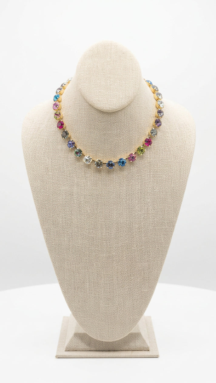 Multicolored rhinestone necklace with round pink, purple, blue, green, and clear stones in gold-tone settings on a beige display bust