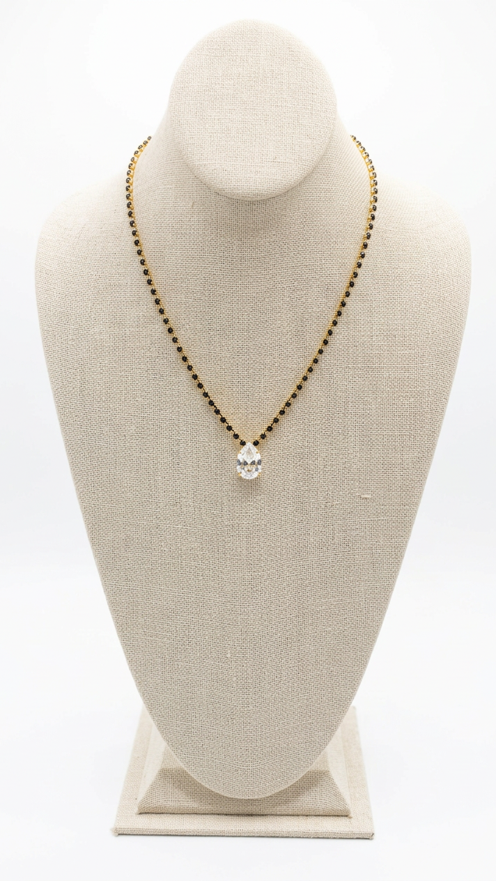 A gold beaded necklace with a small silver-toned pendant displayed on a beige fabric jewelry bust.