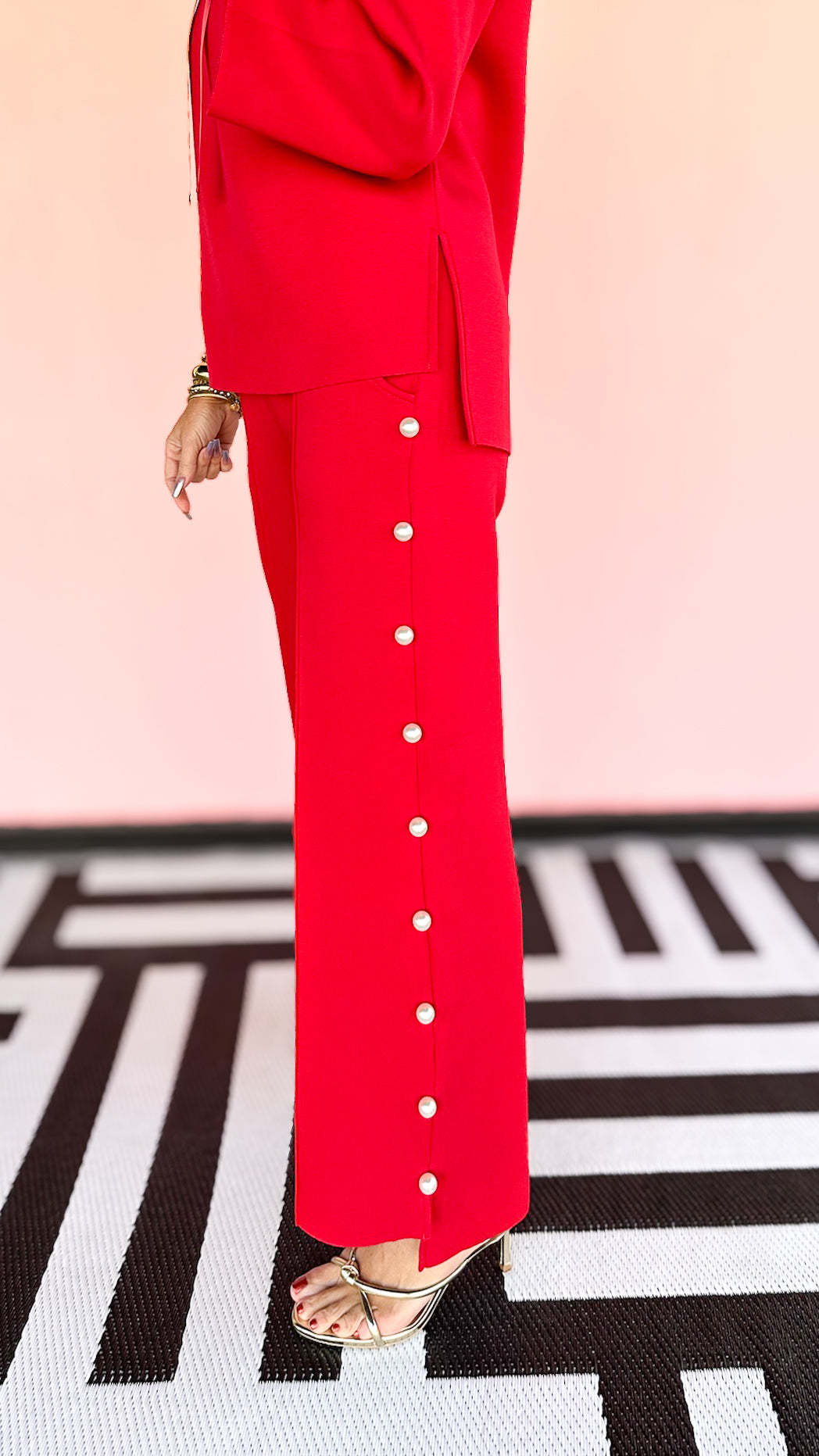 A close-up of a red pant with pearl trim down the leg, featuring a small pocket on the side.