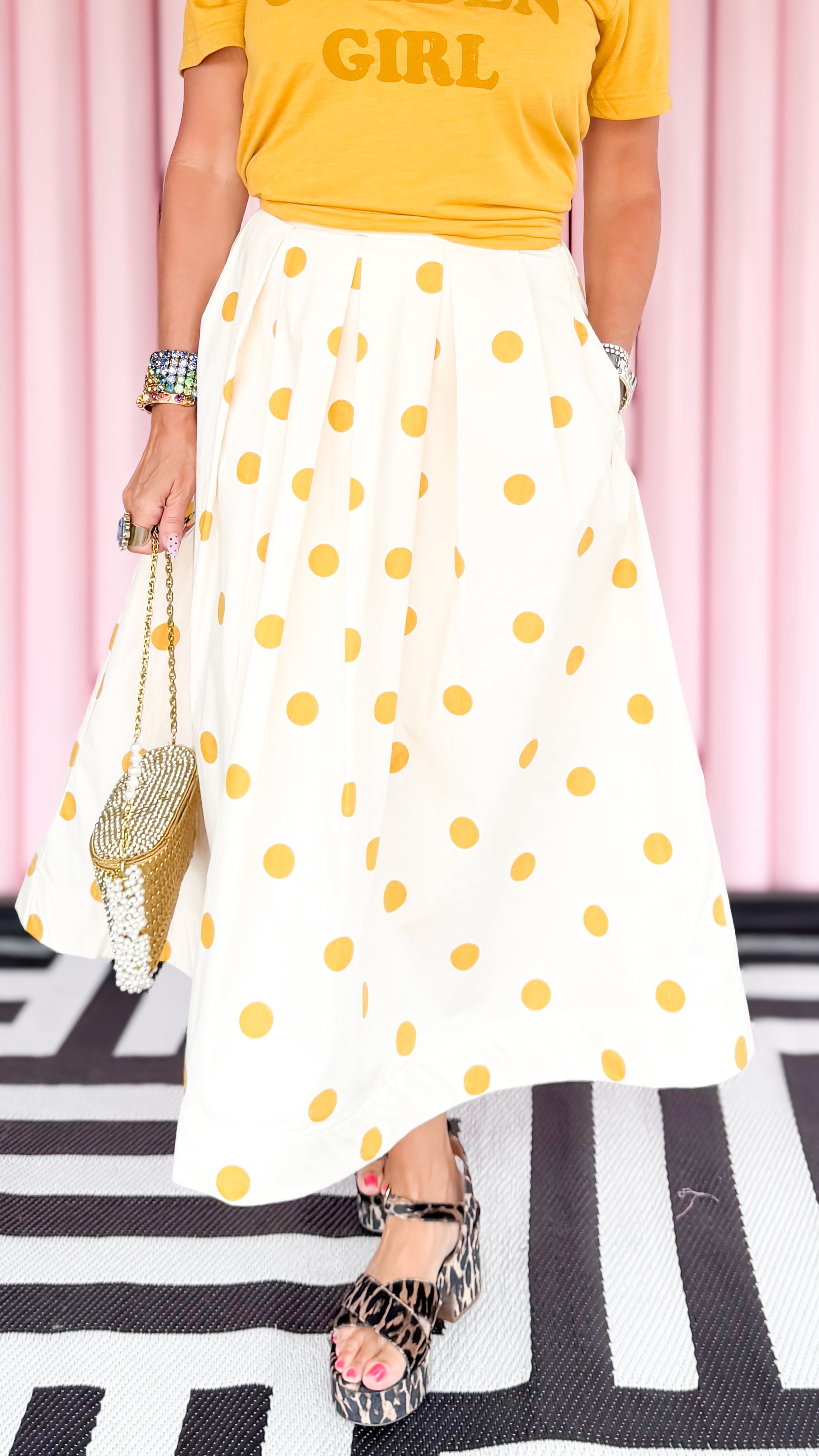 Woman wearing a yellow t-shirt and white polka dot skirt with a pink curtain background