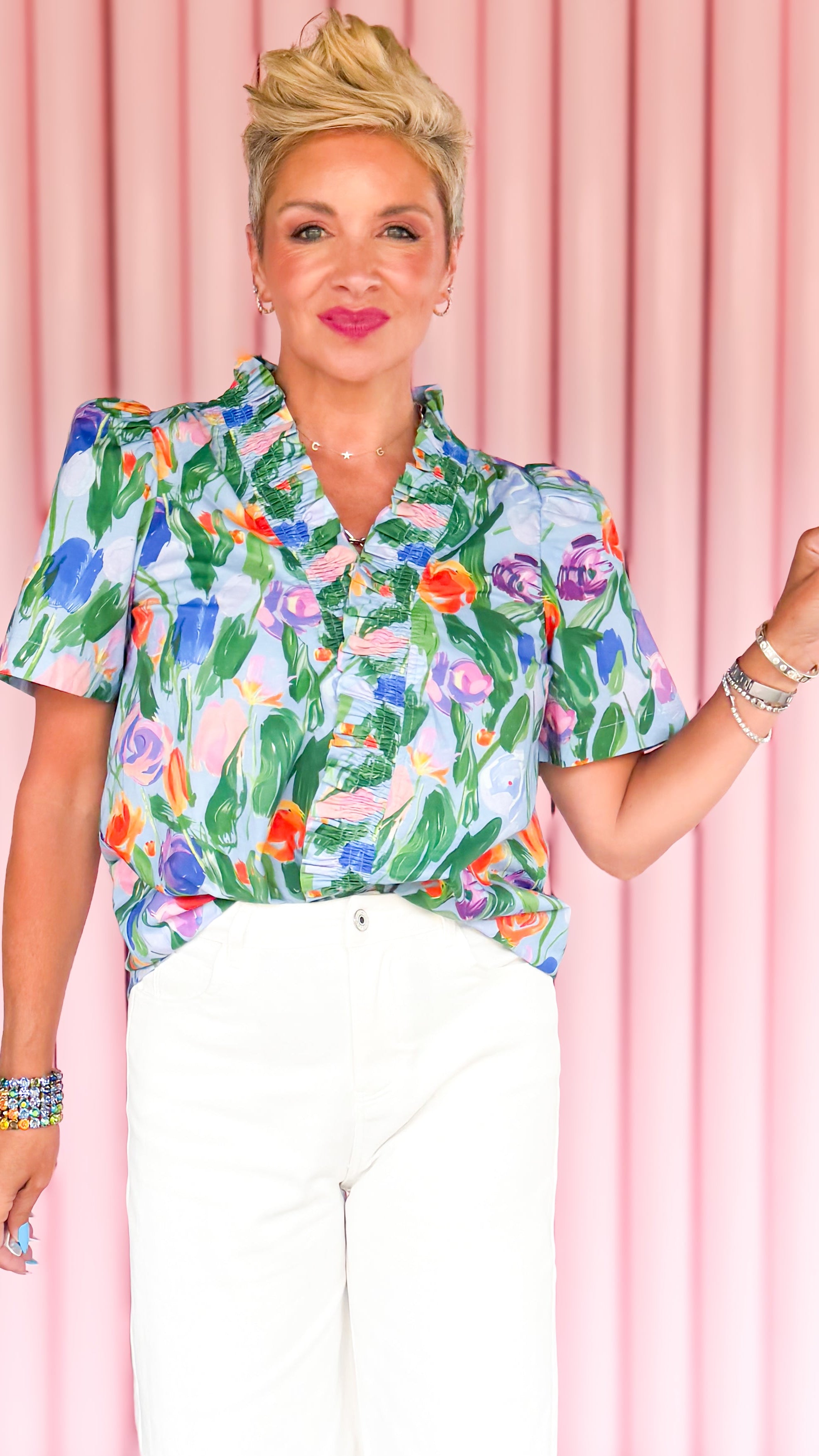 Woman wearing a colorful floral blouse and white pants against a pink and black geometric background
