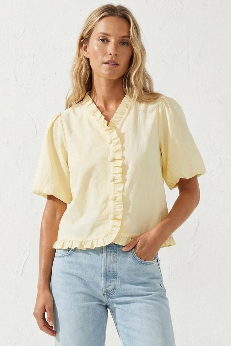 Woman wearing a yellow blouse with short sleeves and light blue jeans against a white background