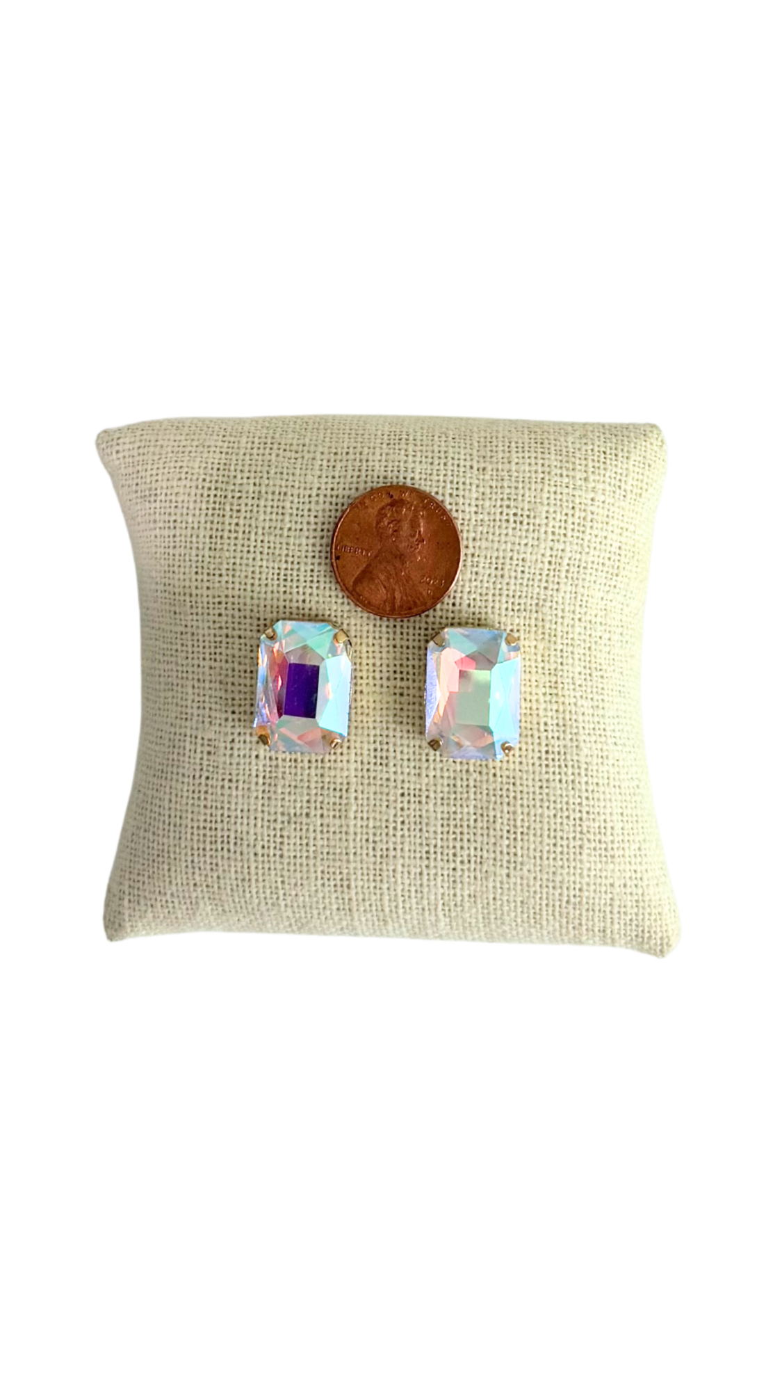 Pair of earrings on a beige fabric cushion with a penny for scale.