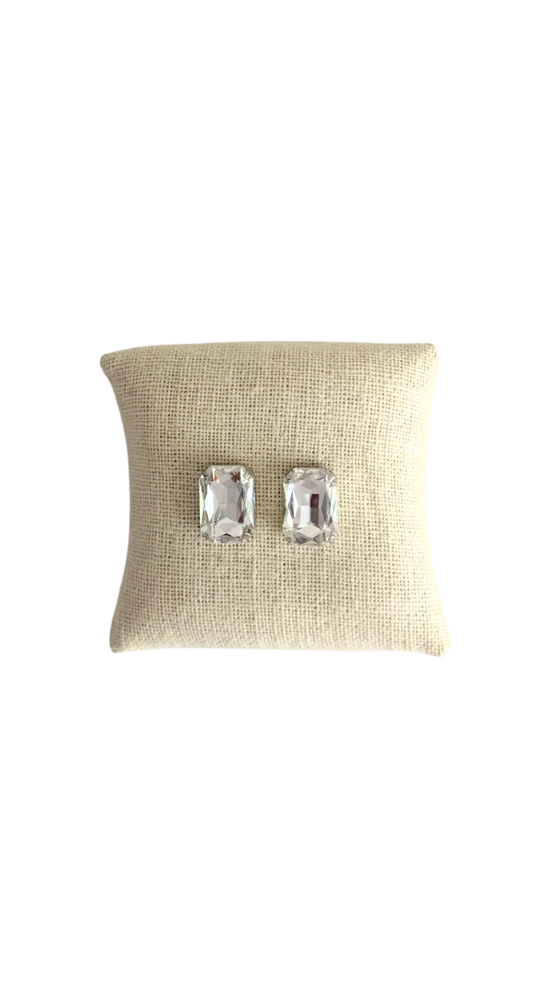 Pair of silver earrings on a textured beige pillow against a white background