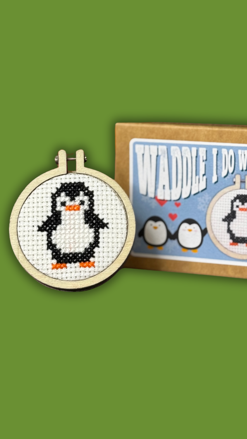 Cross-stitch mini kit with penguin design and packaging on a green background