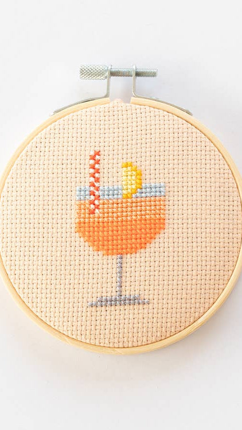 Cross-stitched design of a cocktail glass with a lemon wedge in a wooden hoop on a white background
