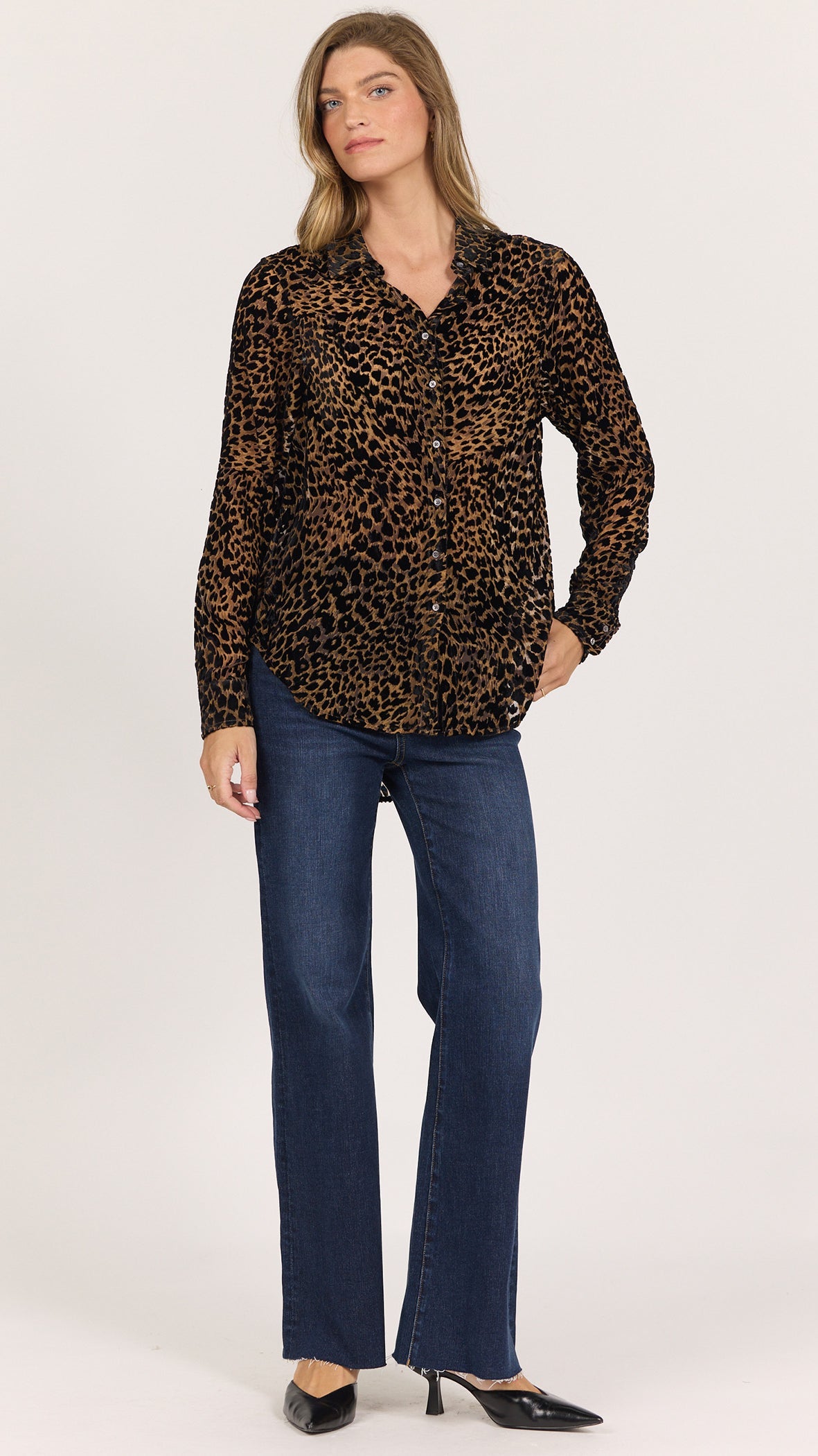 Full-length front view of Dear John Lolita leopard print button up shirt in noir panthera worn untucked with dark wash flare jeans and black heels
