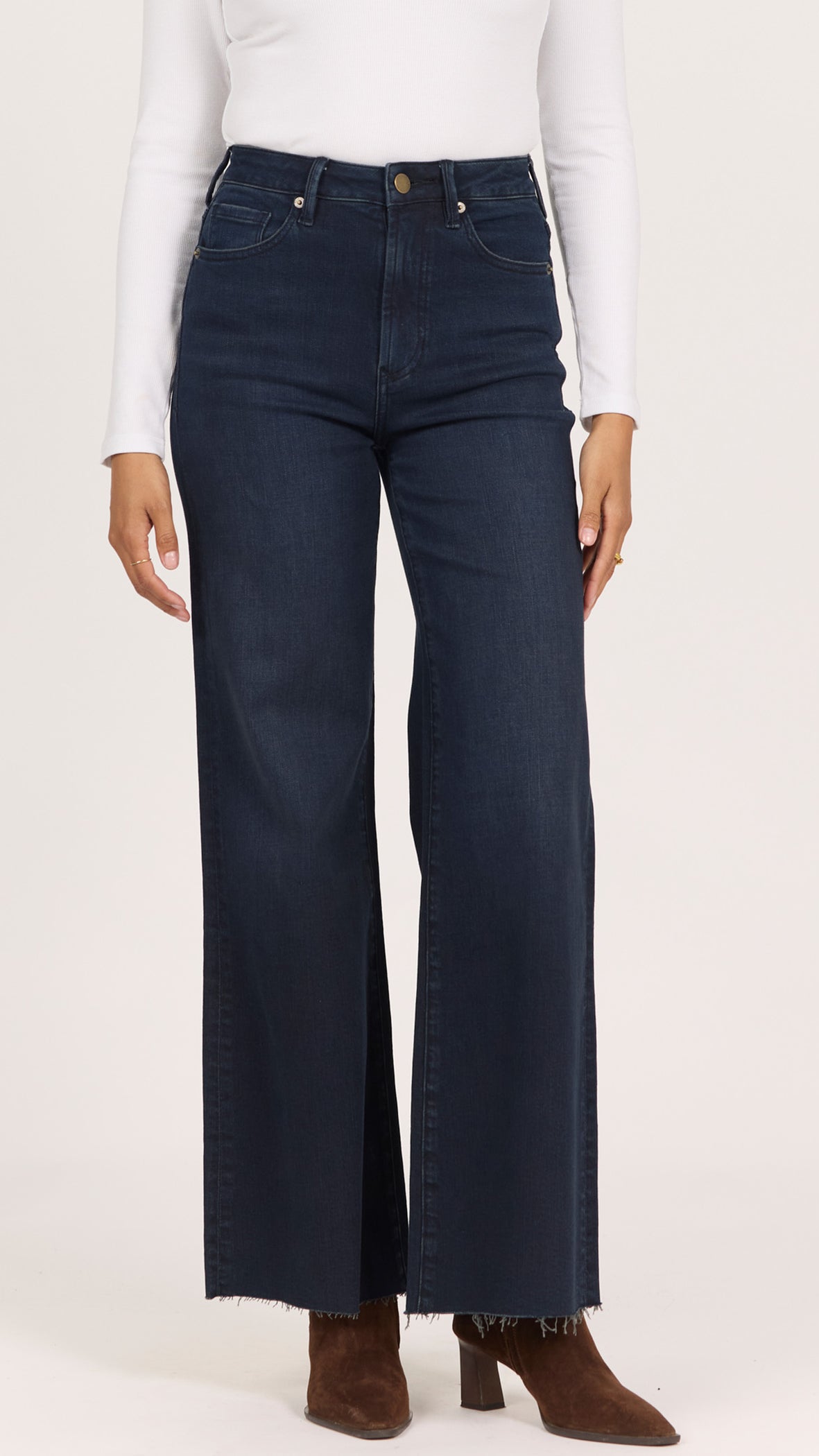 Front view of inkwell dark wash Fiona jeans showing the high rise, button closure and frayed raw cut hem over brown suede boots