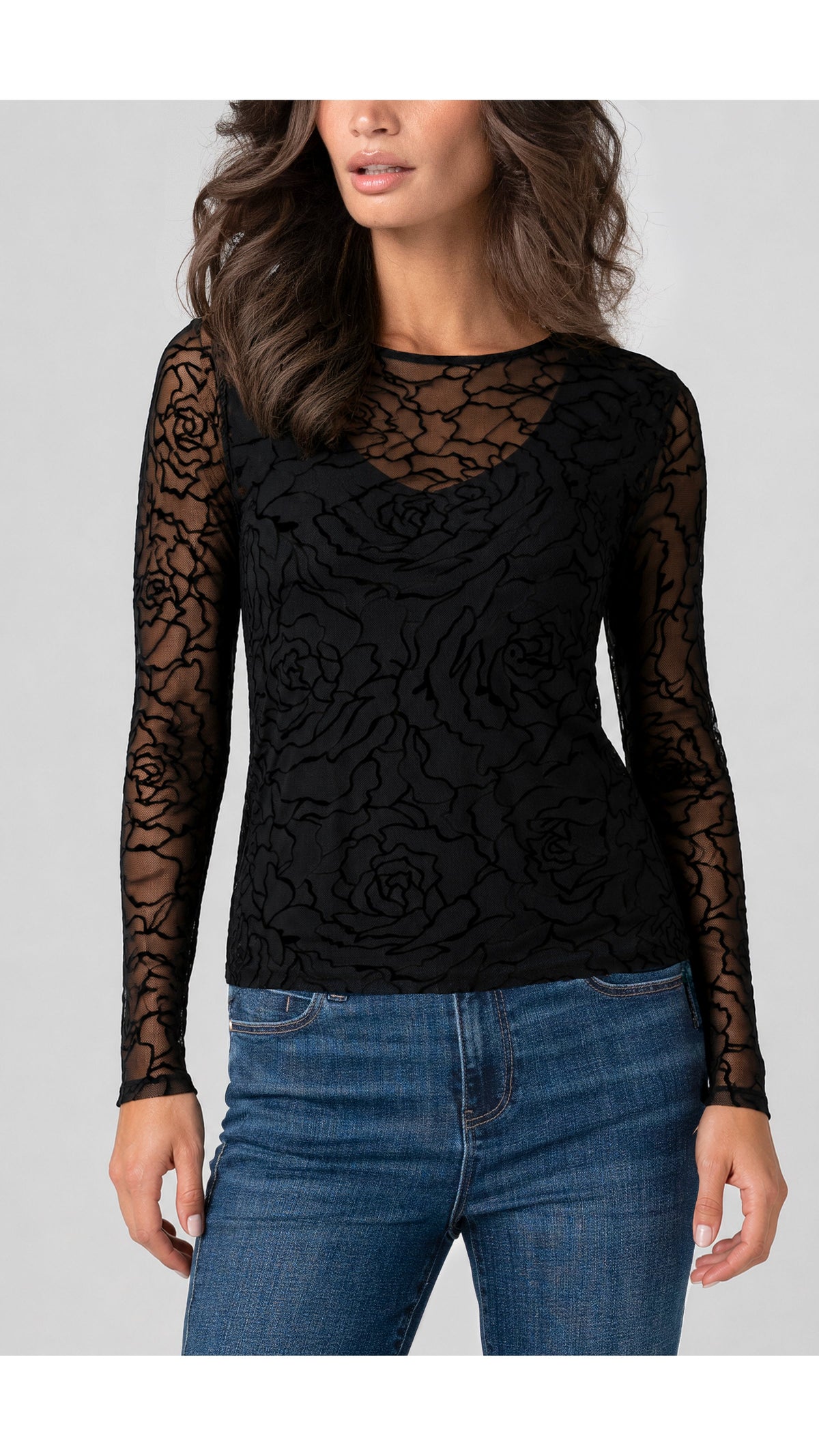 Model wearing black rose embroidered sheer mesh layered top untucked over blue jeans, front view