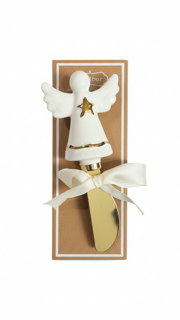 A hand holds a white ceramic angel-shaped knife server with gold trim and a gold knife blade, wrapped in a white ribbon and presented on its brown kraft box.