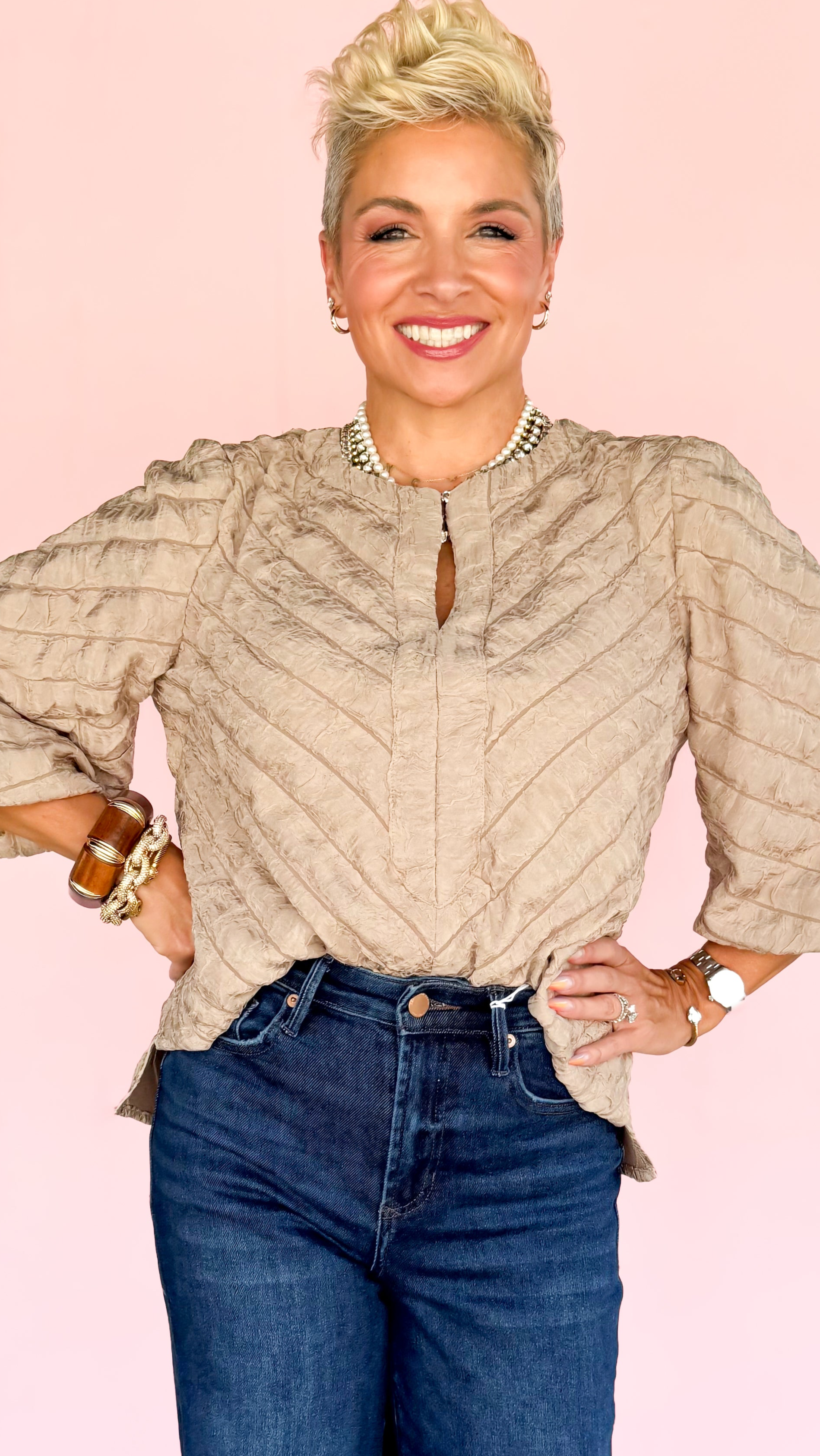 Woman wearing a beige blouse and blue jeans against a pink background