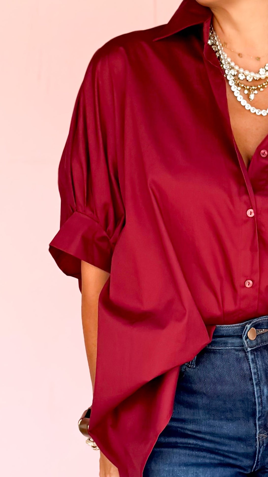 Woman wearing a red blouse and blue jeans on a patterned floor with a pink wall.