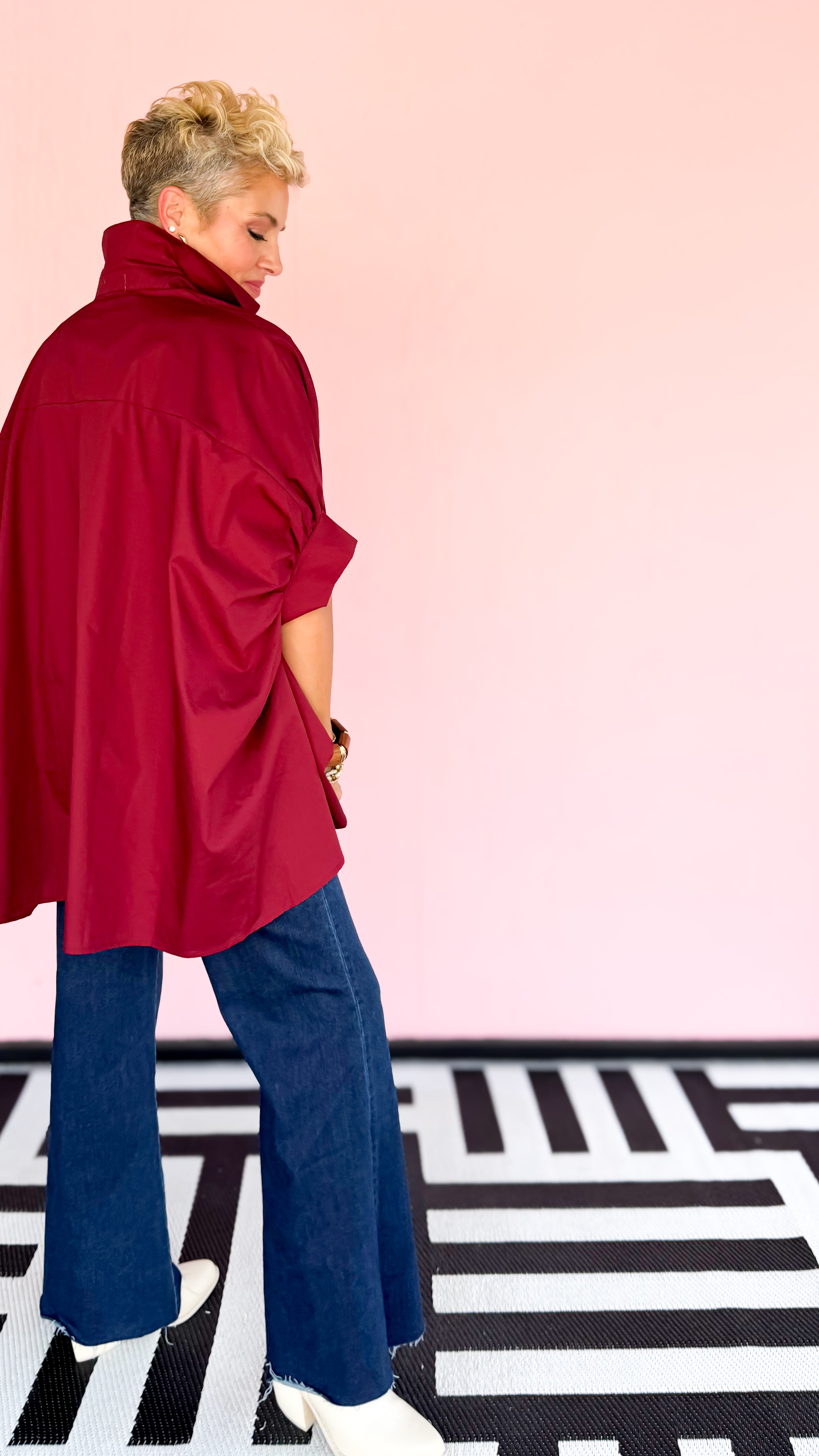 Woman wearing a red blouse and blue jeans on a patterned floor with a pink wall.