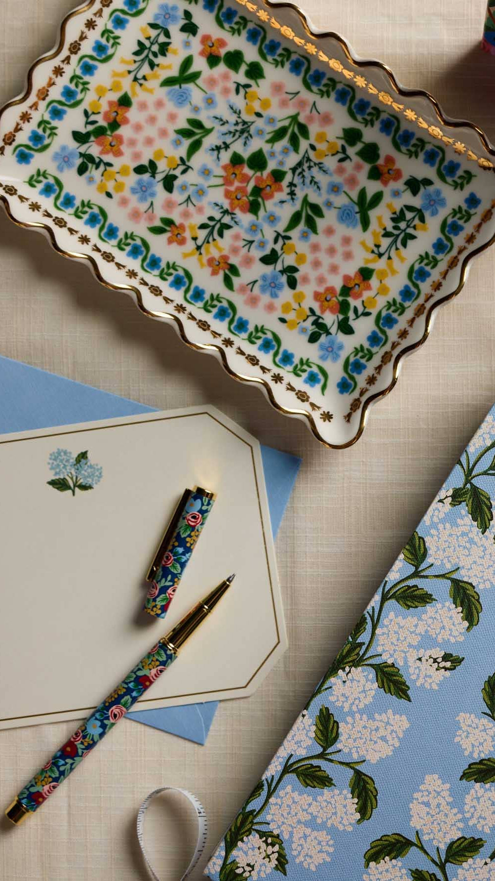 Floral stationery items including a pen, paper, and notebook on a textured surface.