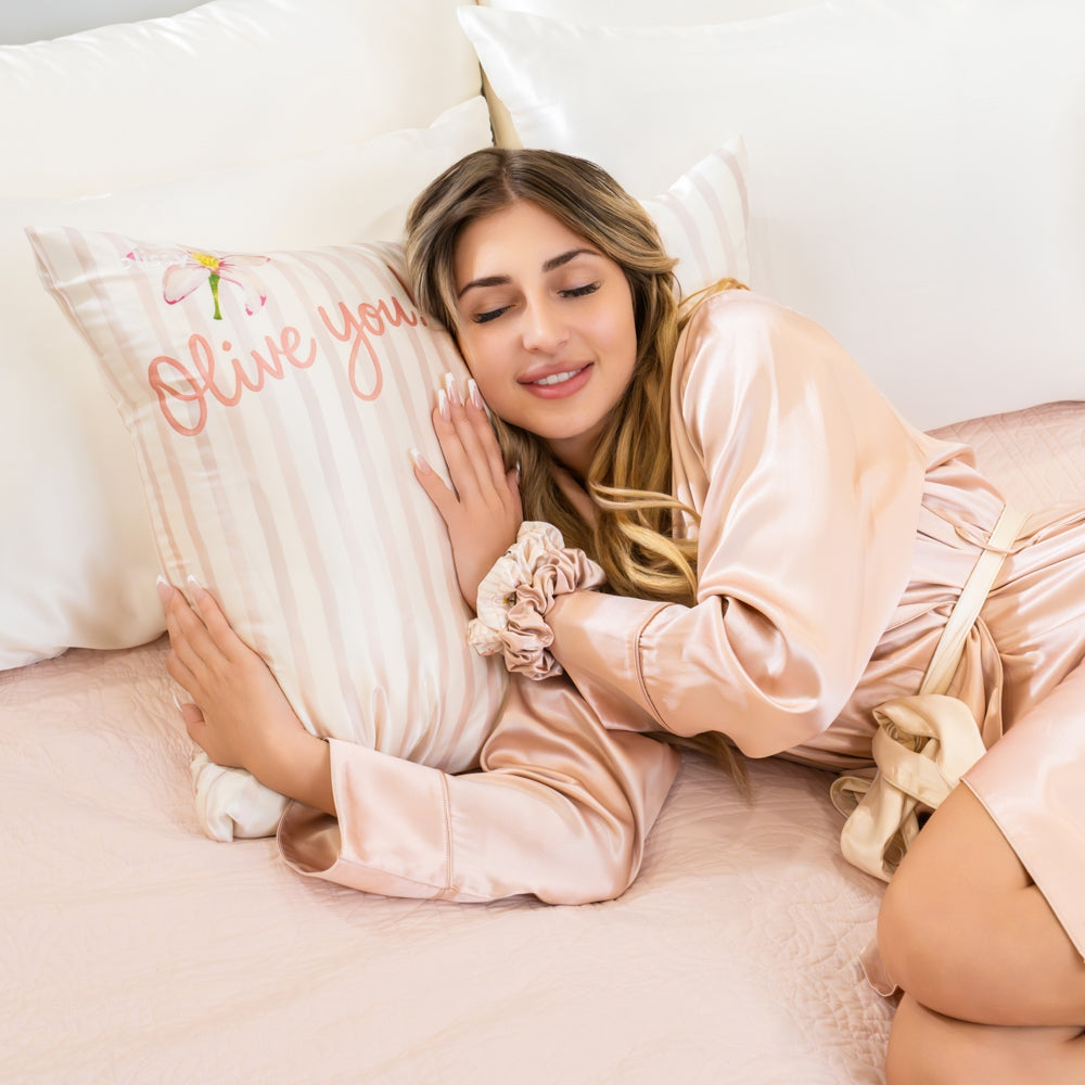 Woman in a satin robe holding a pillow with 'I love you' text on a bed.