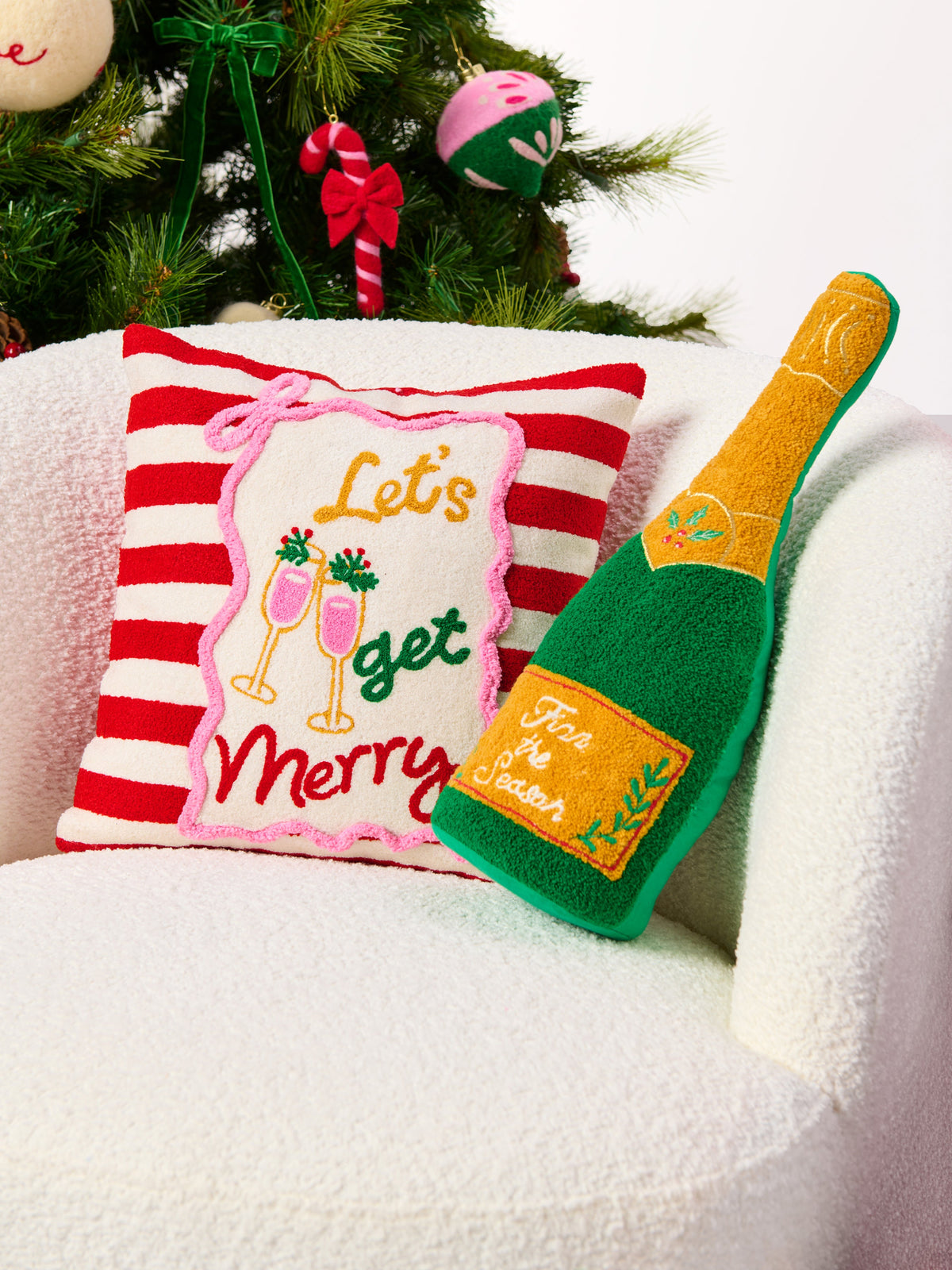 Shiraleah Fizz The Season Champagne Bottle Pillow in green and gold, tufted cotton-polyester, styled on a white armchair, lifestyle view