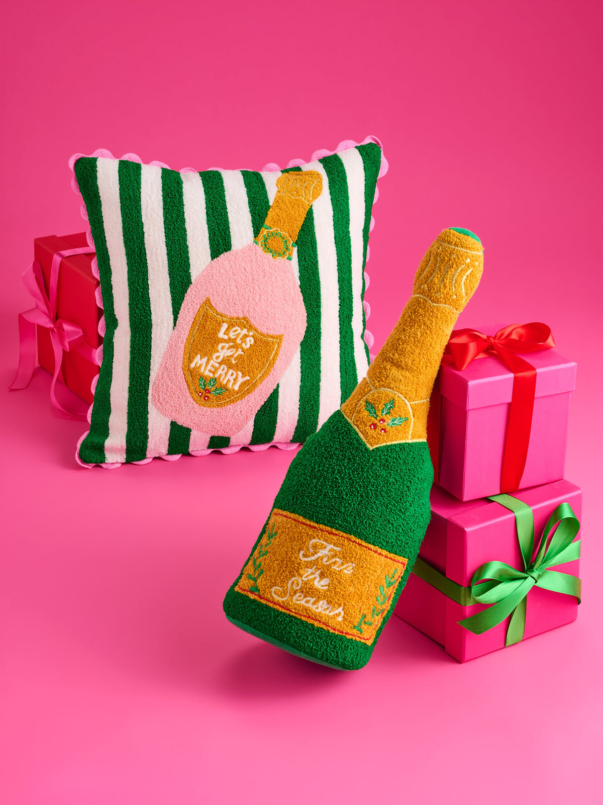 Shiraleah Fizz The Season Champagne Bottle Pillow in green and gold, tufted cotton-polyester, styled with gifts on a pink backdrop, lifestyle view