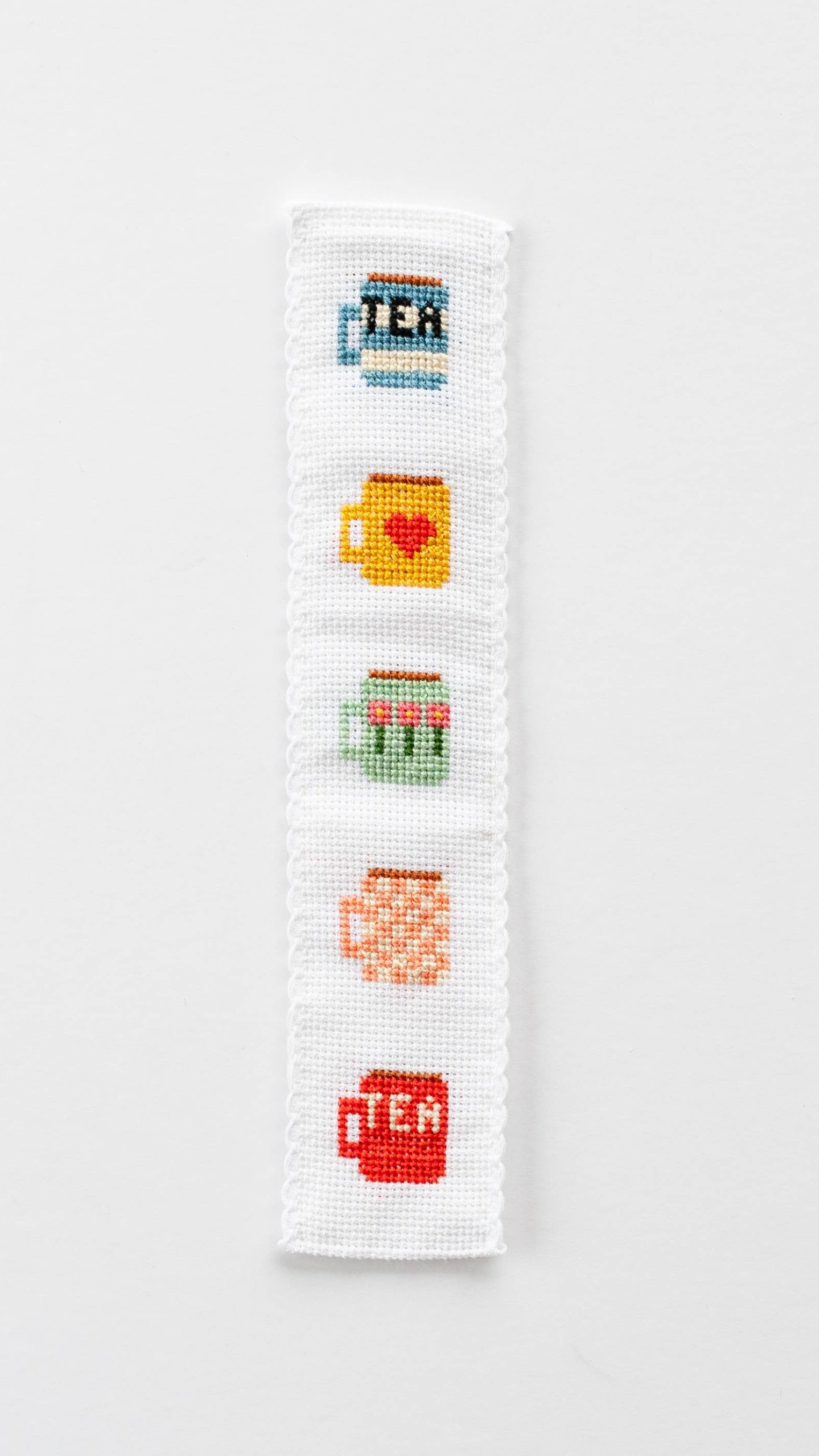 Cross-stitched bookmark with tea-themed designs on a white background