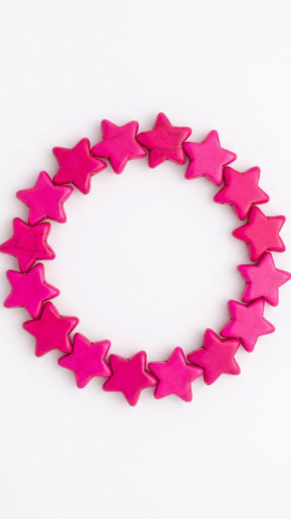 A pink elastic bracelet made of small star-shaped links, resting on a light beige desk surface.