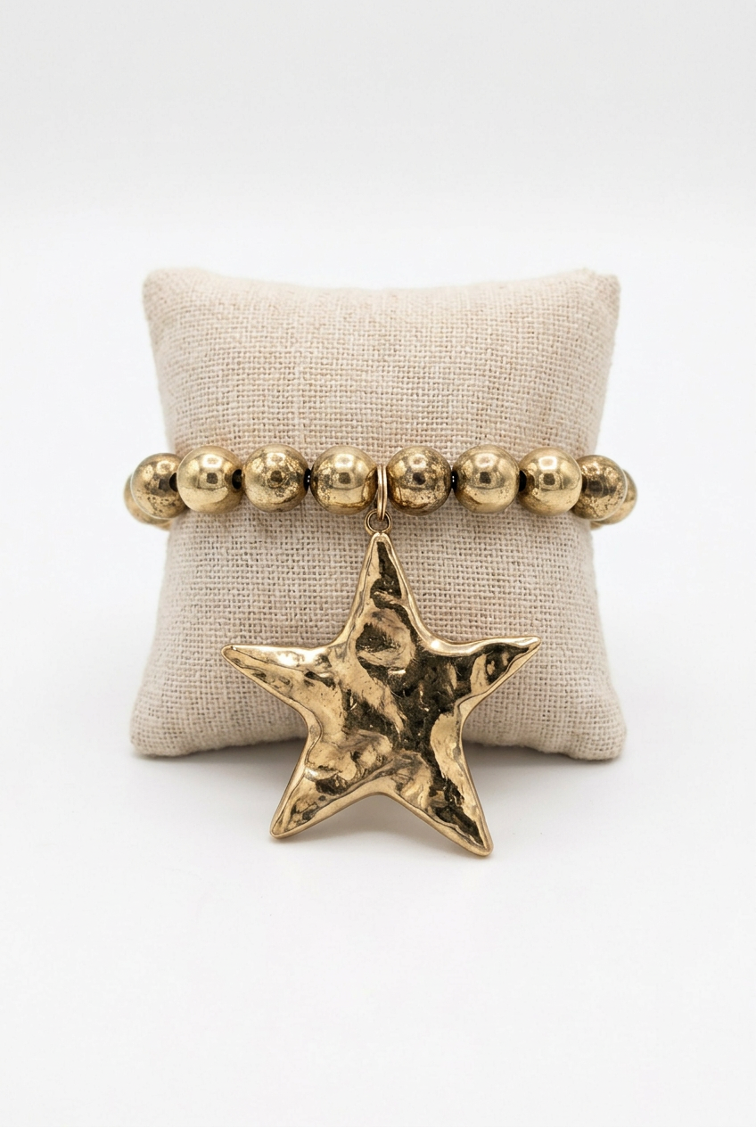 Accessories to Go gold-tone beaded bracelet with a large hammered star charm on a linen pillow