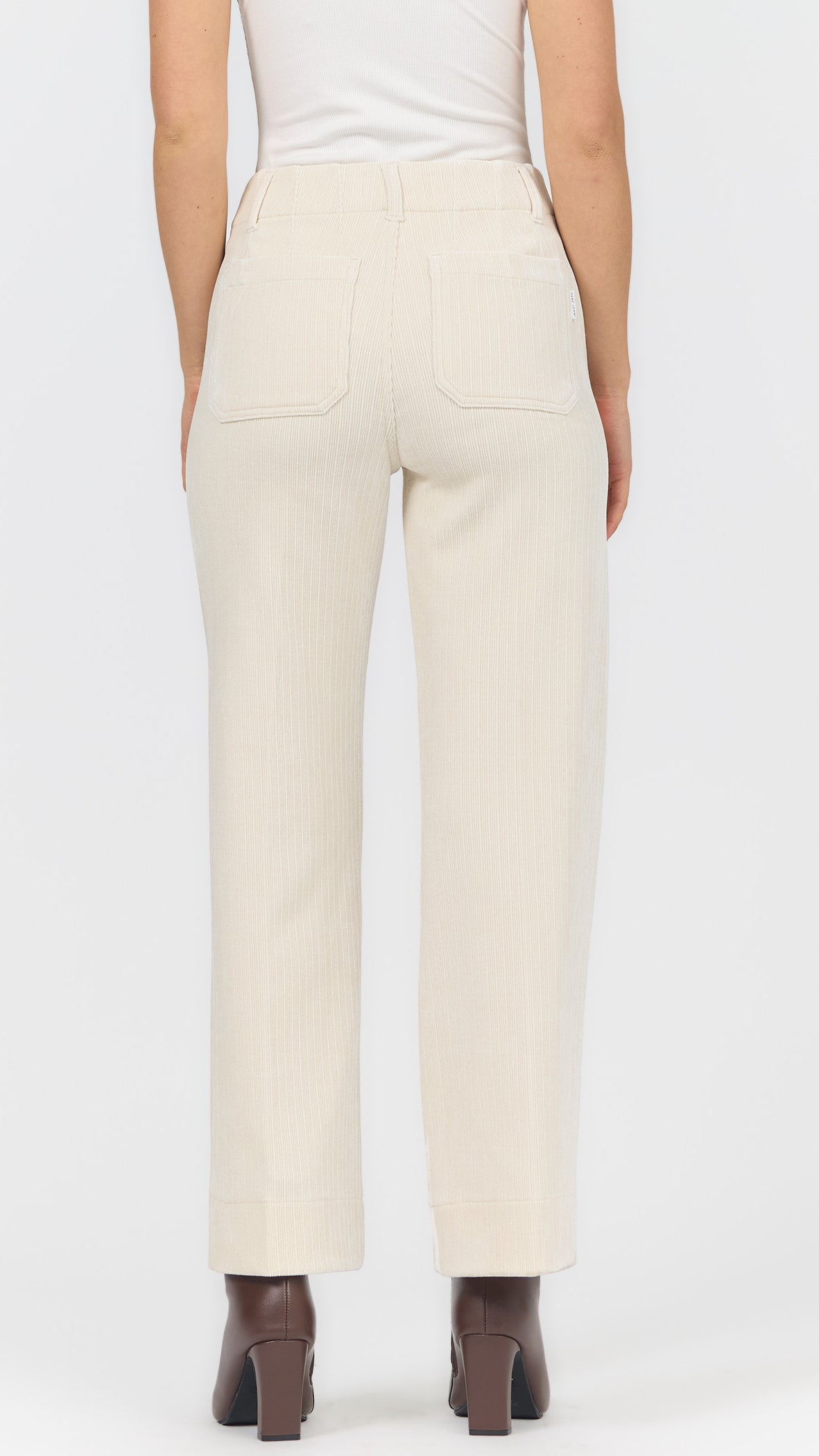 Back view of egret corduroy wide leg pants showing the back patch pockets and brown heeled ankle boots