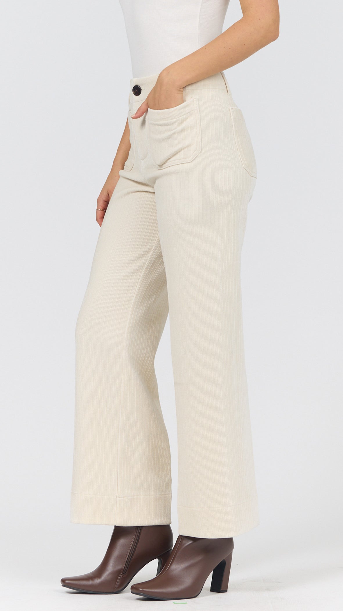 Three-quarter side view of egret corduroy wide leg pants with a hand in the front pocket and brown heeled ankle boots