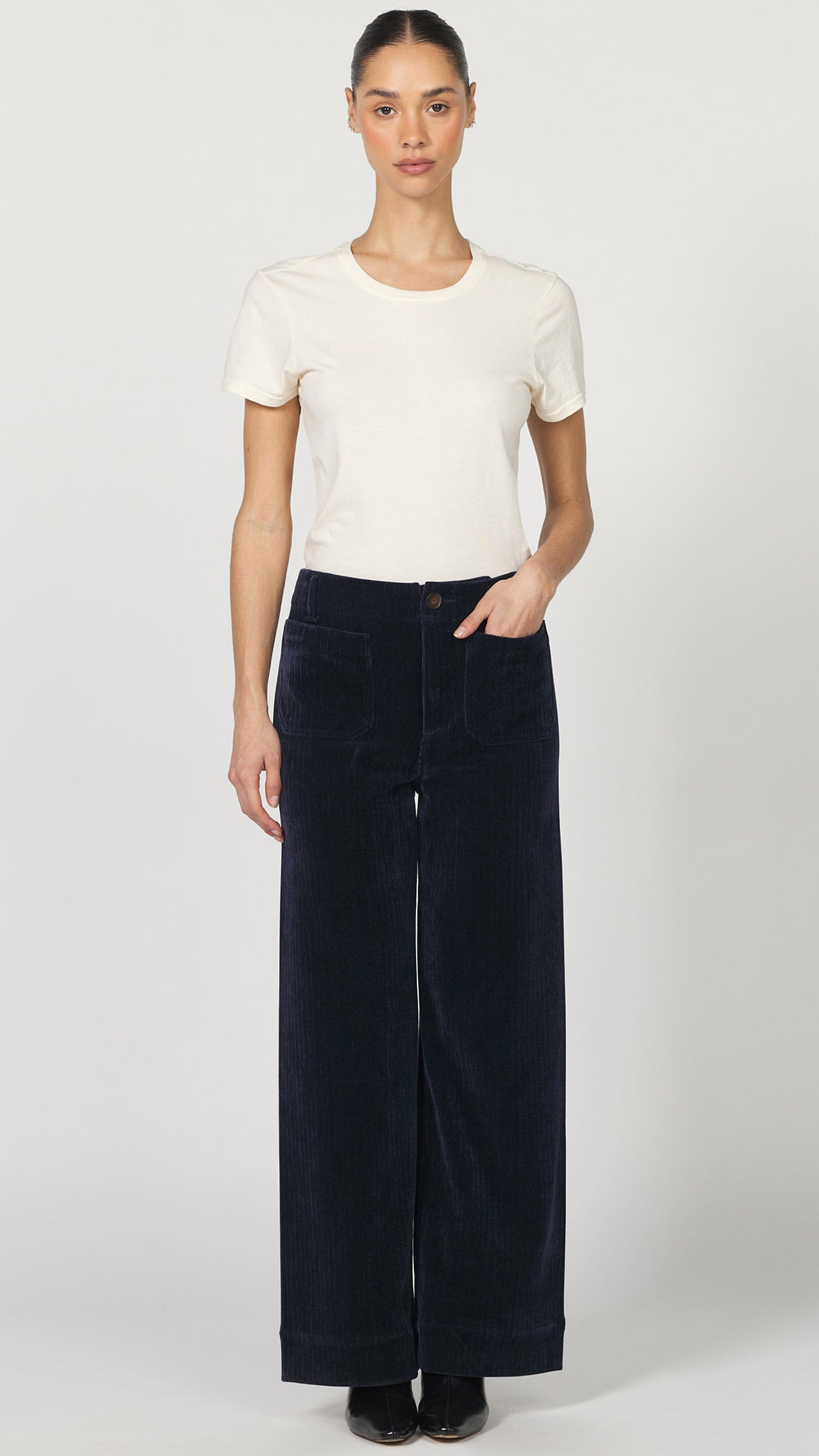 Full-length front view of Dear John Audrey black iris corduroy wide leg pants with a tucked cream tee and black pointed heels