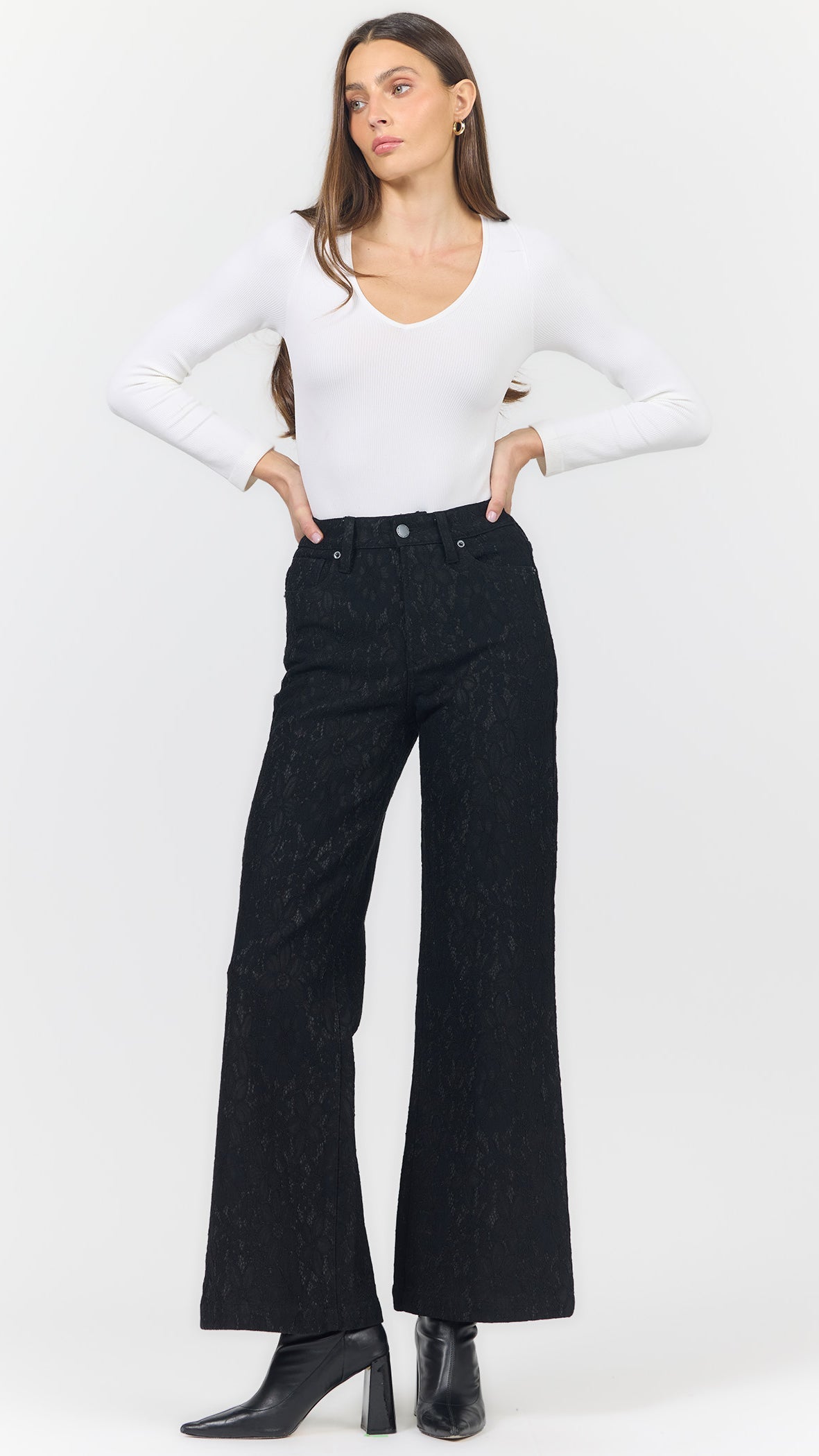 Full-length front view of Dear John Fiona black lace wide leg pants with a white V-neck long sleeve top, hands on hips, and black ankle boots