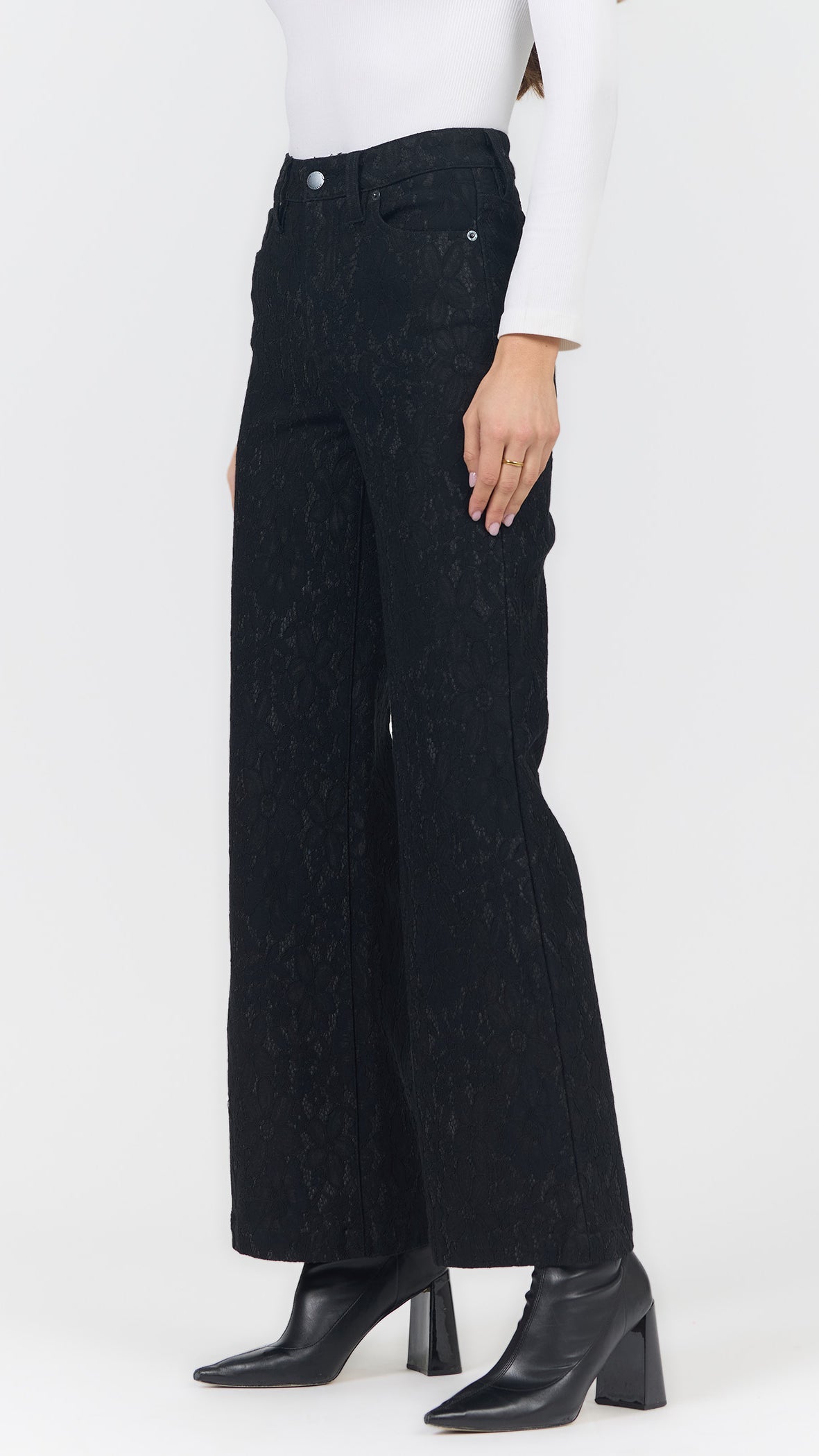 Side view of black lace wide leg pants with a white long sleeve top and black heeled ankle boots