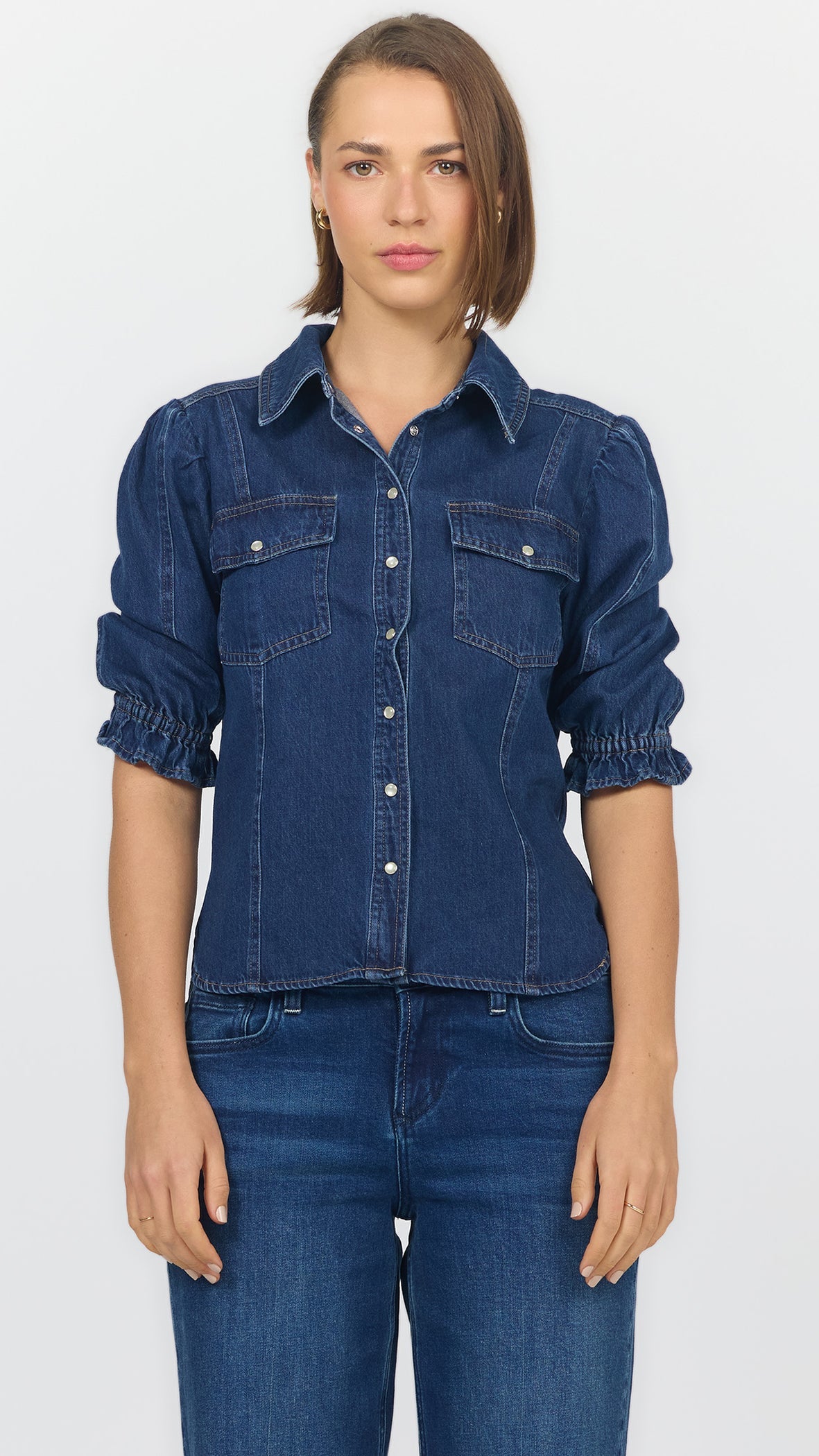 Front view of dark cobalt denim blouse with a pointed collar, flap chest pockets, puffed shoulders, and ruffled elbow cuffs